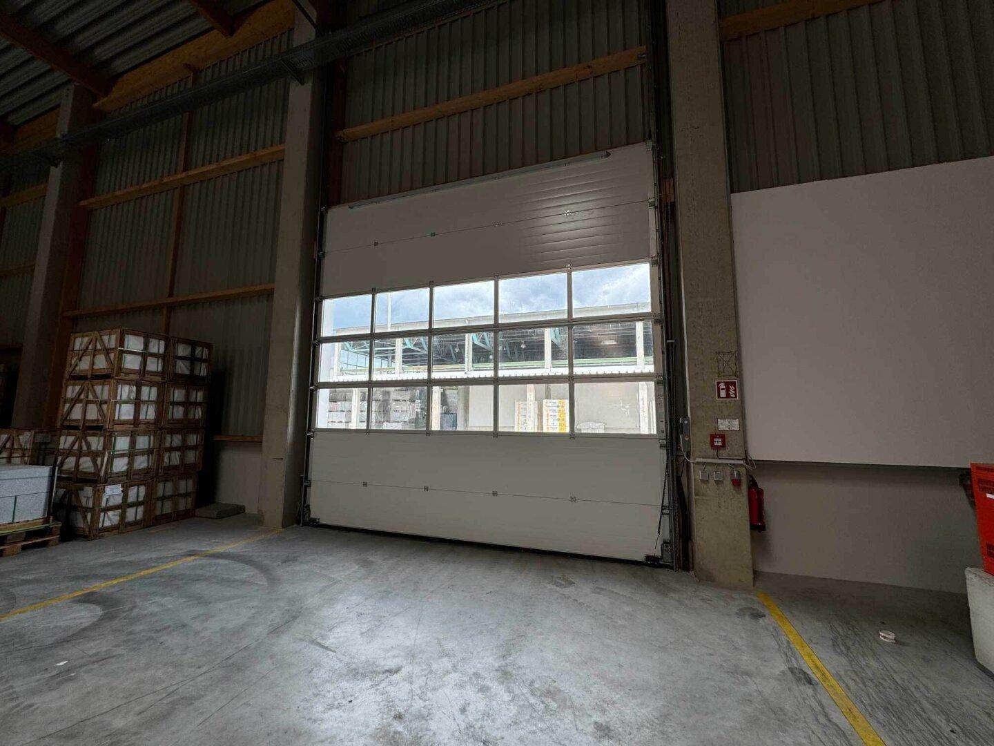 Großes Sektionaltor mit Fenstern in einer Lagerhalle, das viel Tageslicht hereinlässt und eine helle Atmosphäre schafft.