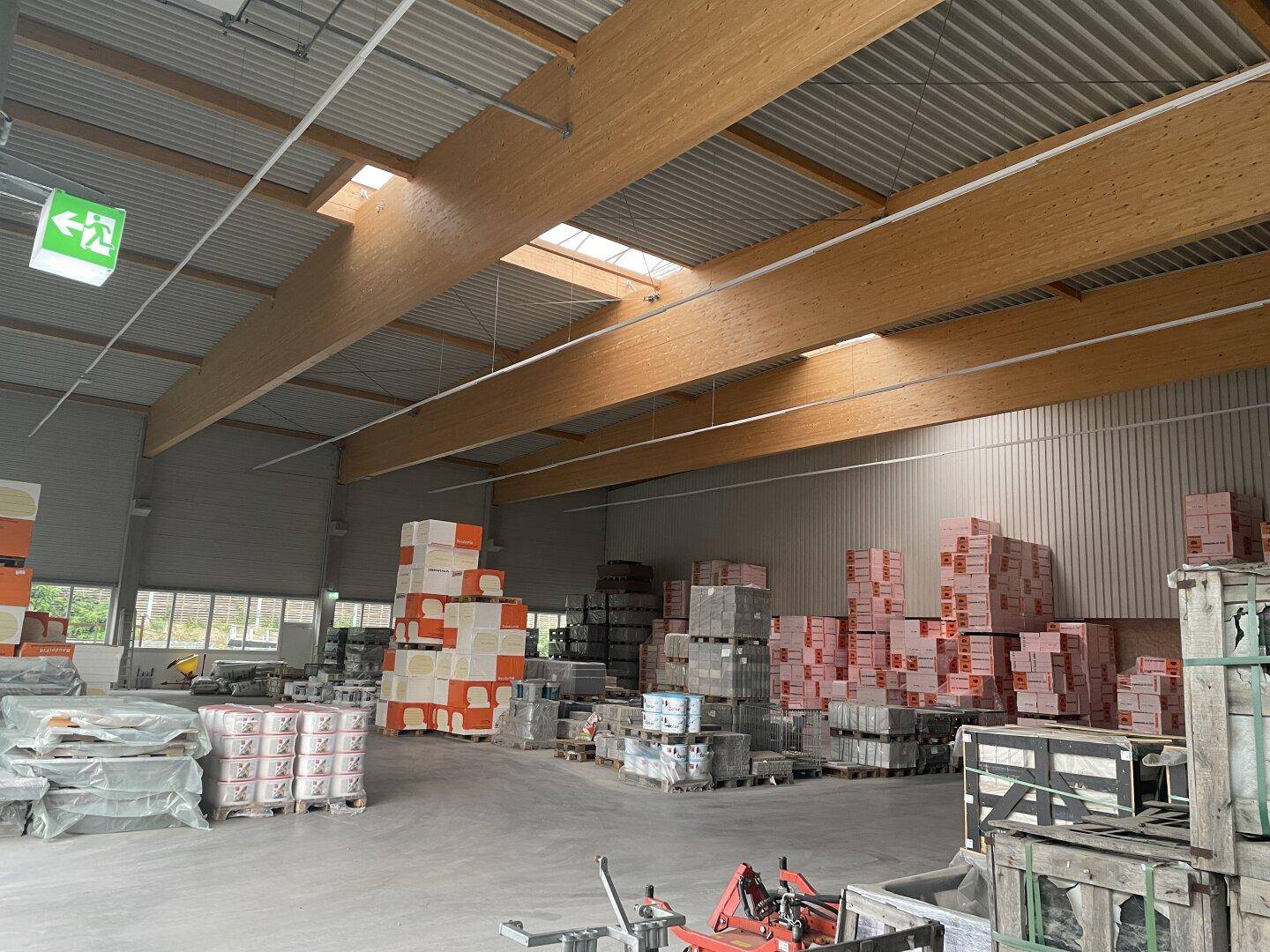 Geräumige Lagerhalle mit hohen Decken, sichtbaren Holzträgern und Oberlichtern, gefüllt mit Baumaterialien.
