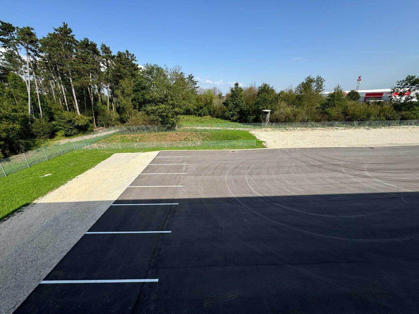 Großer Parkplatz mit markierten Stellflächen, umgeben von Grünflächen und Bäumen.