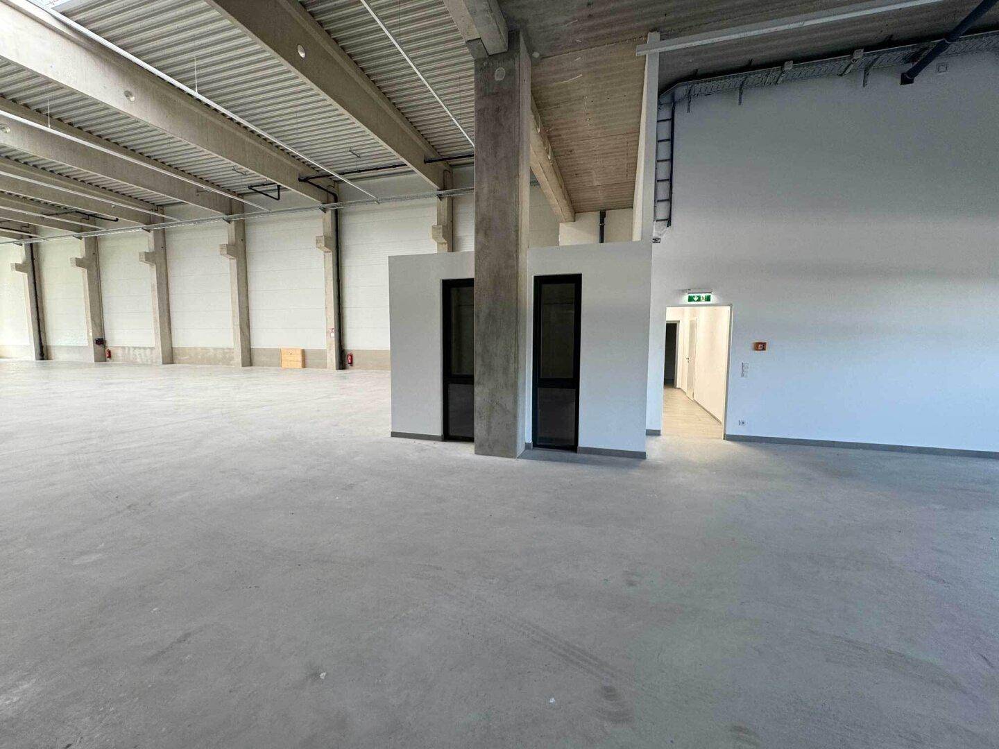 Große, leere Lagerhalle mit Betonboden, hohen Decken und sichtbaren Trägerstrukturen.
