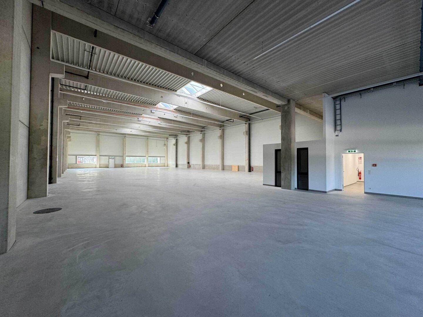 Weitläufige Lagerhalle mit Betonboden, Oberlichtern und hohen Decken, bereit zur Nutzung.