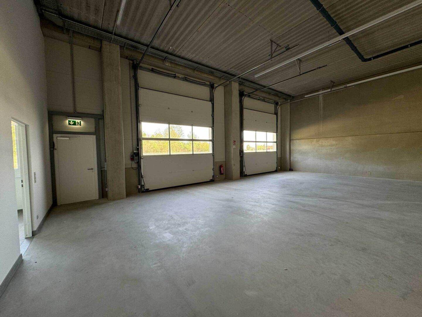 Geräumige Lagerhalle mit Betonboden und zwei großen Rolltoren für den Zugang.