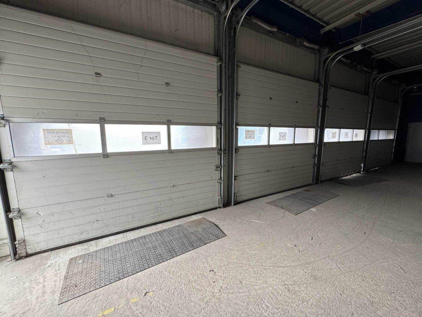 Mehrere große Rolltore mit kleinen Fenstern in einer industriellen Ladezone.