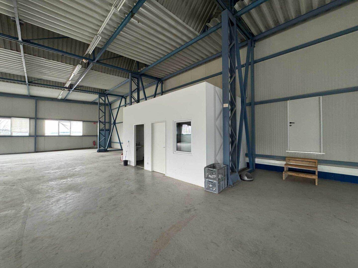 Weitläufige Lagerhalle mit Betonboden und zwei kleinen, abgetrennten Räumen.