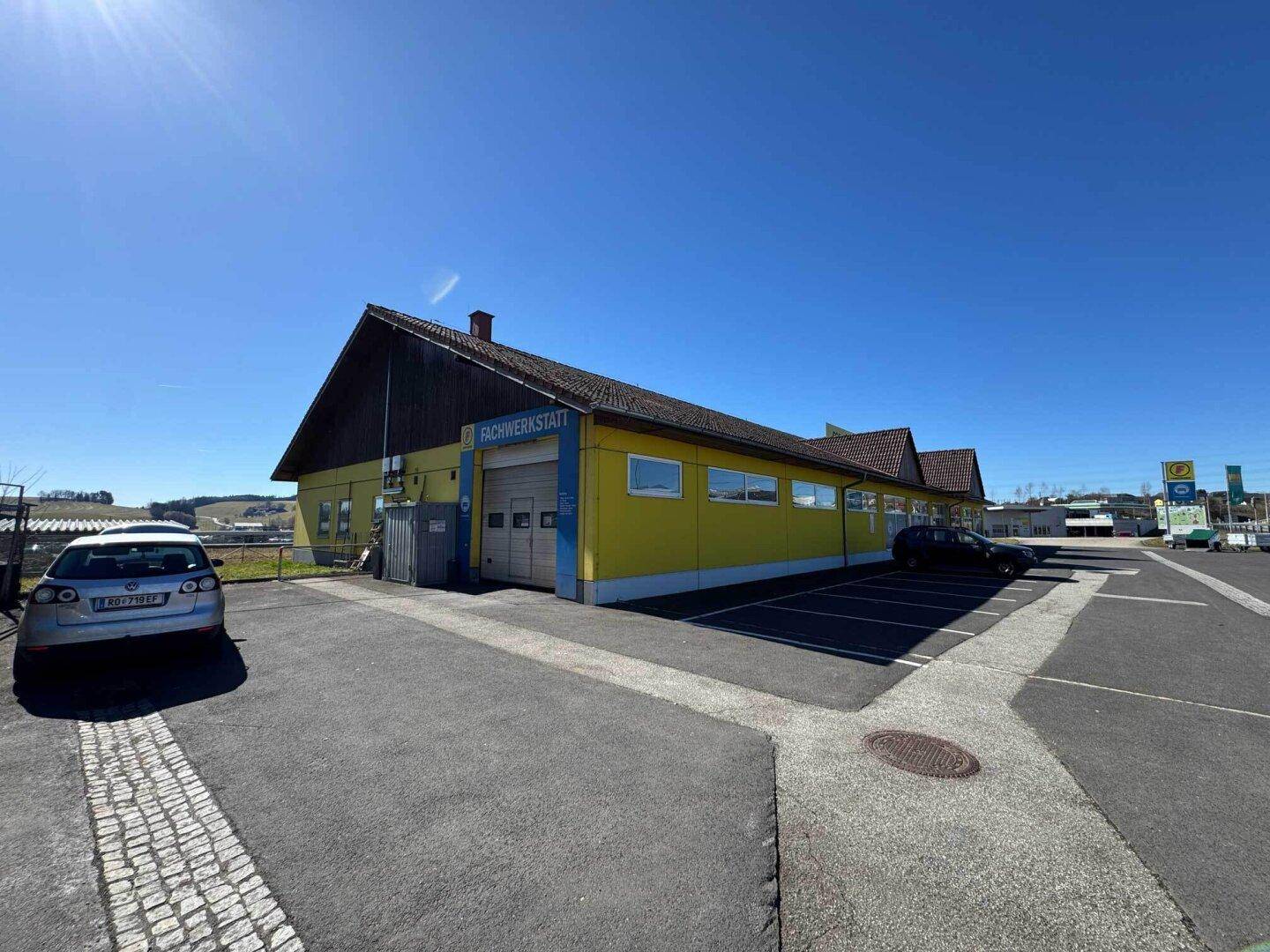 Rückseite des Geschäftsgebäudes mit Werkstattzugang und weiteren Parkplätzen unter klarem Himmel.