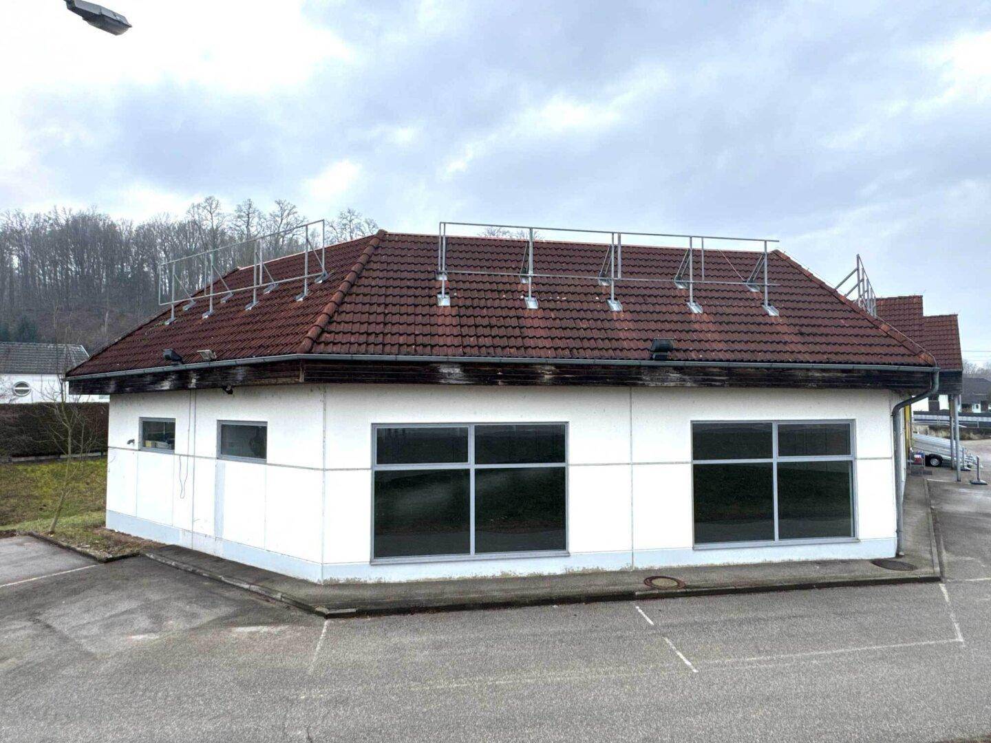 Eckansicht des Gewerbegebäudes mit weißer Fassade, roten Ziegeln und mehreren Fenstern.