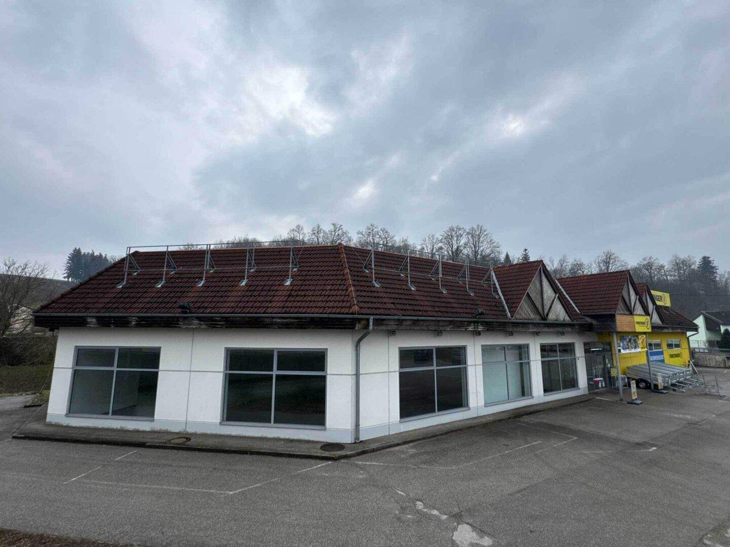 Ansicht des Gewerbegebäudes mit weißer Fassade, großen Fenstern und einem roten Ziegeldach.