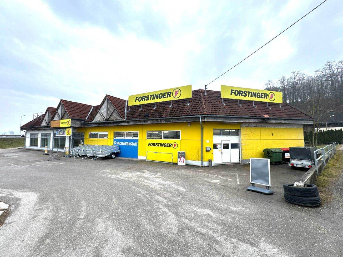 Rückseite des Gewerbegebäudes mit gelber Fassade, Laderampe und Müllcontainern.