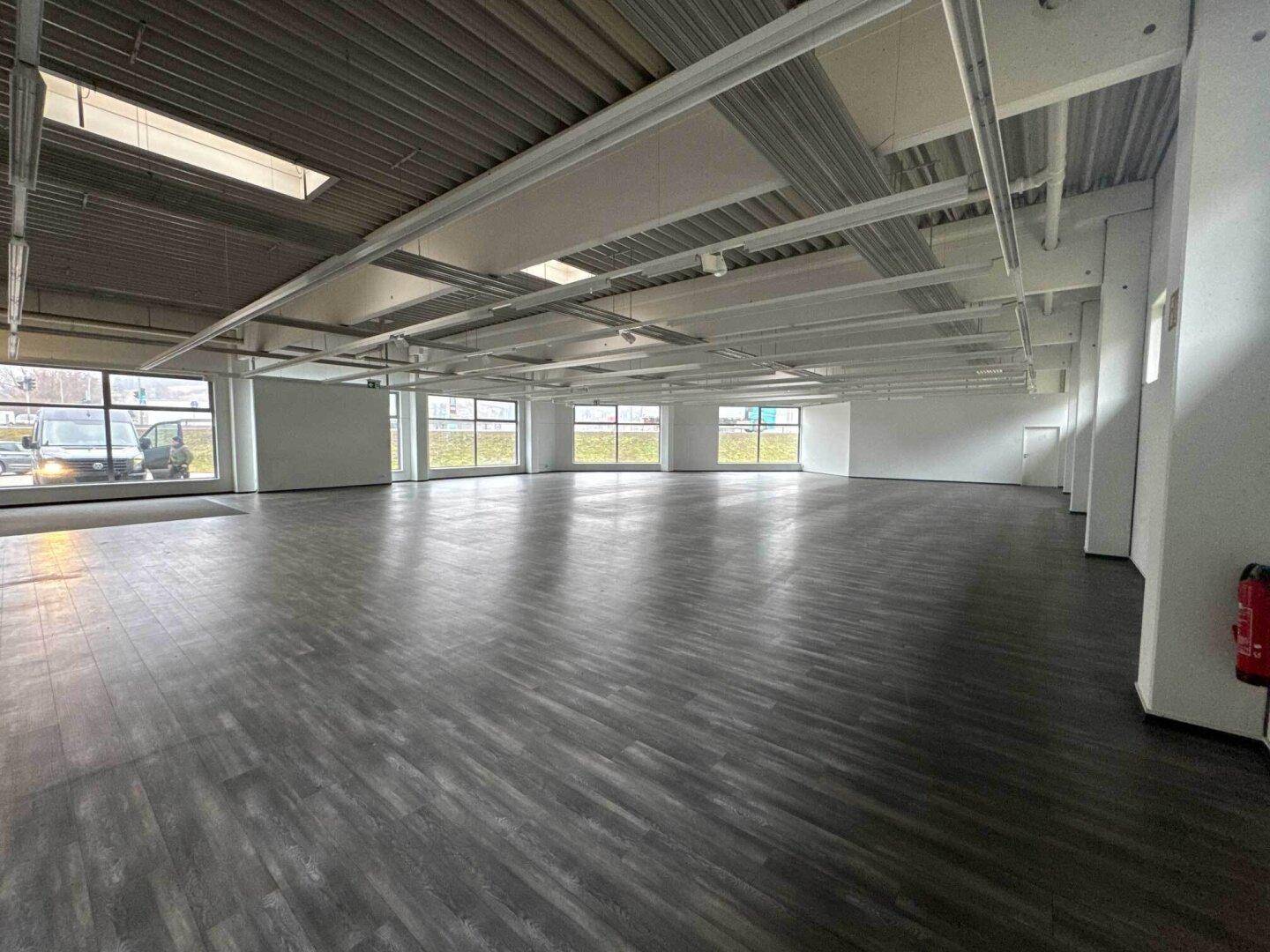 Großer, offener Gewerberaum mit dunklem Laminatboden, hohen Decken und vielen Fenstern.