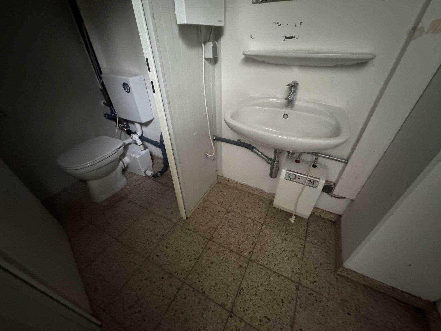 Kleiner Toilettenraum mit Waschbecken, WC und gefliestem Boden in einfacher Ausführung.