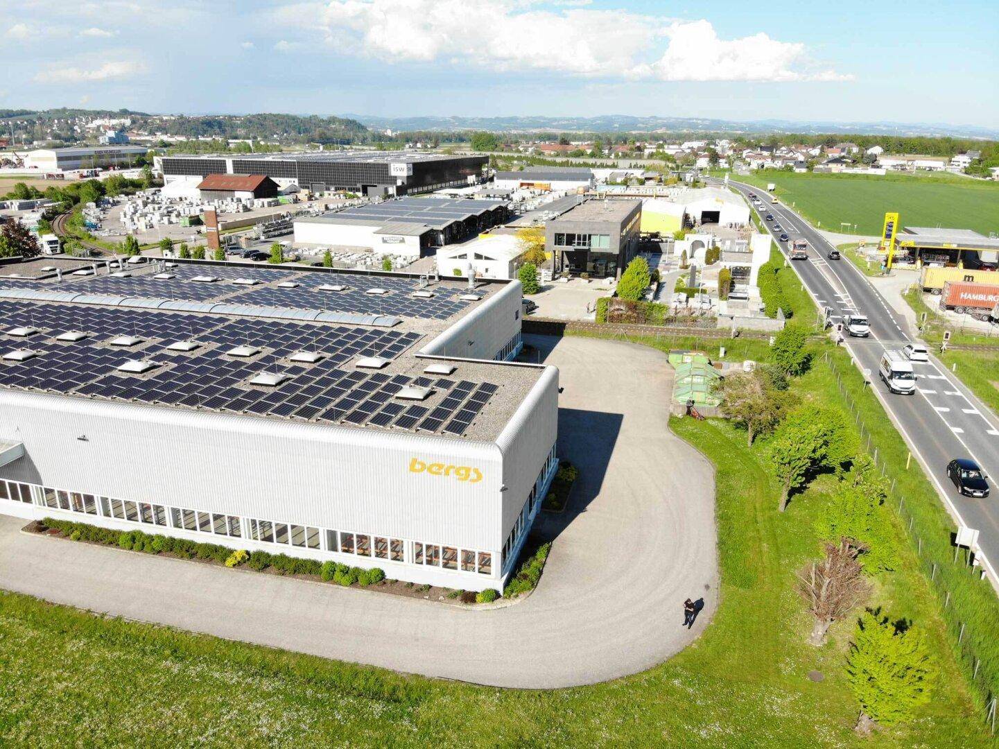 Luftaufnahme eines Industriegebäudes mit Photovoltaikanlage auf dem Dach und angrenzender Straße.