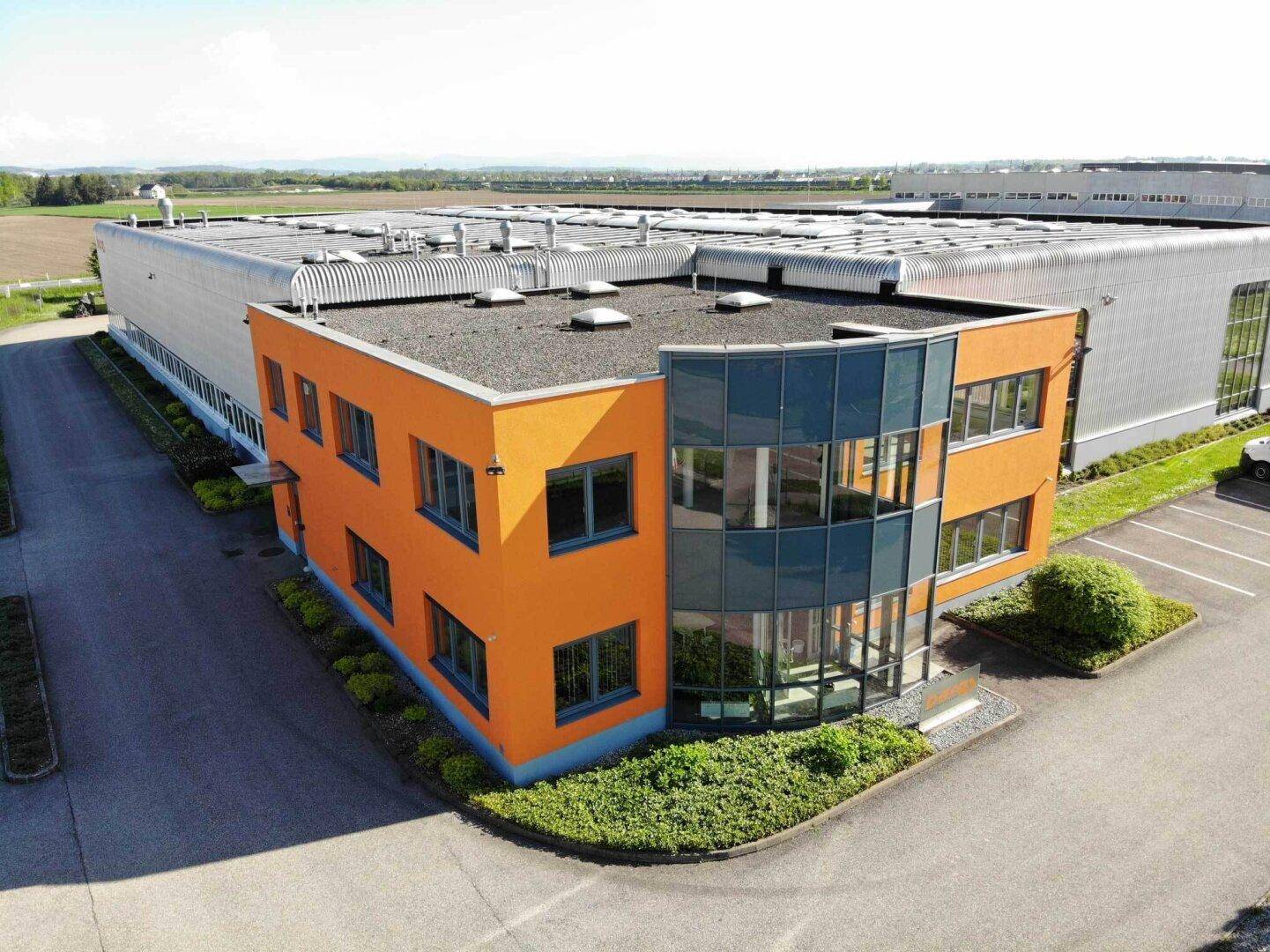 Detailaufnahme des orangefarbenen Bürotrakts eines Industriegebäudes mit moderner Glasfassade.