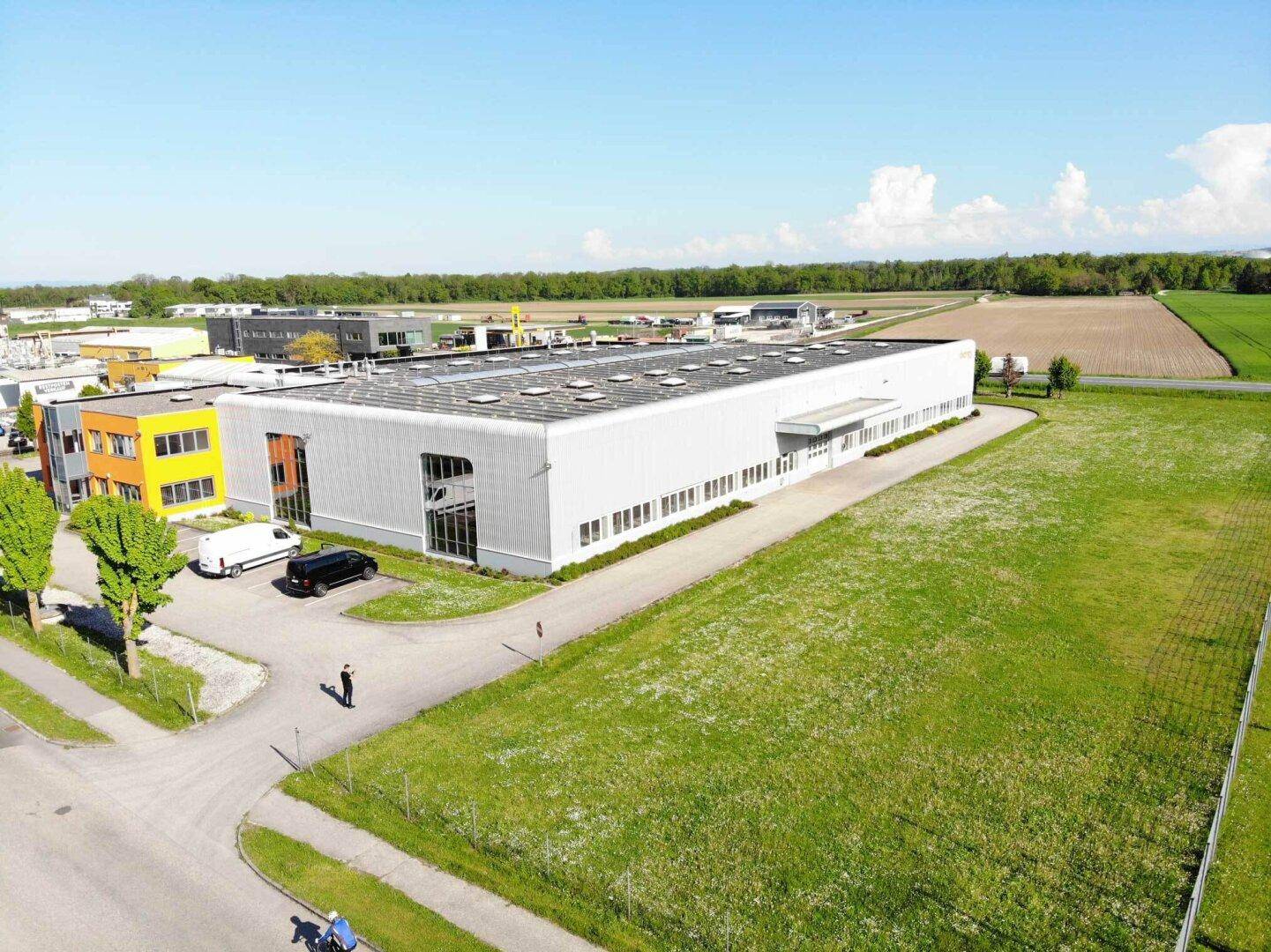Weitläufige Luftaufnahme eines Industriegebäudes mit angrenzenden Feldern und viel Grünfläche.