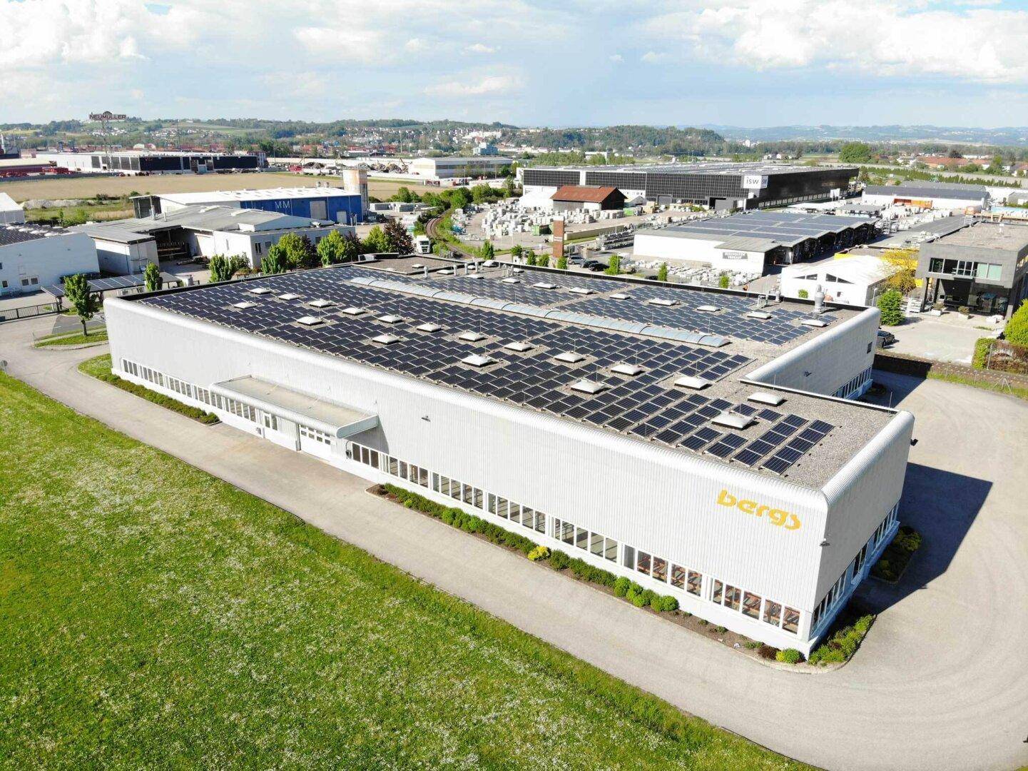 Luftaufnahme eines modernen Industriegebäudes mit umfangreicher Photovoltaikanlage auf dem Dach.