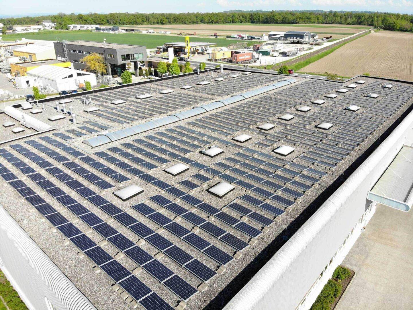 Nahaufnahme der Photovoltaikanlage auf dem Dach eines Industriegebäudes unter blauem Himmel.