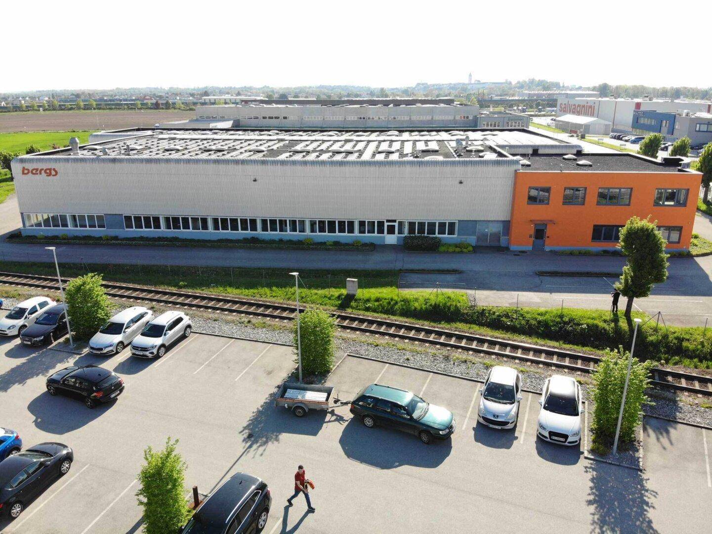 Luftaufnahme eines Industriegebäudes mit orangefarbenem Bürotrakt und großem Parkplatz.