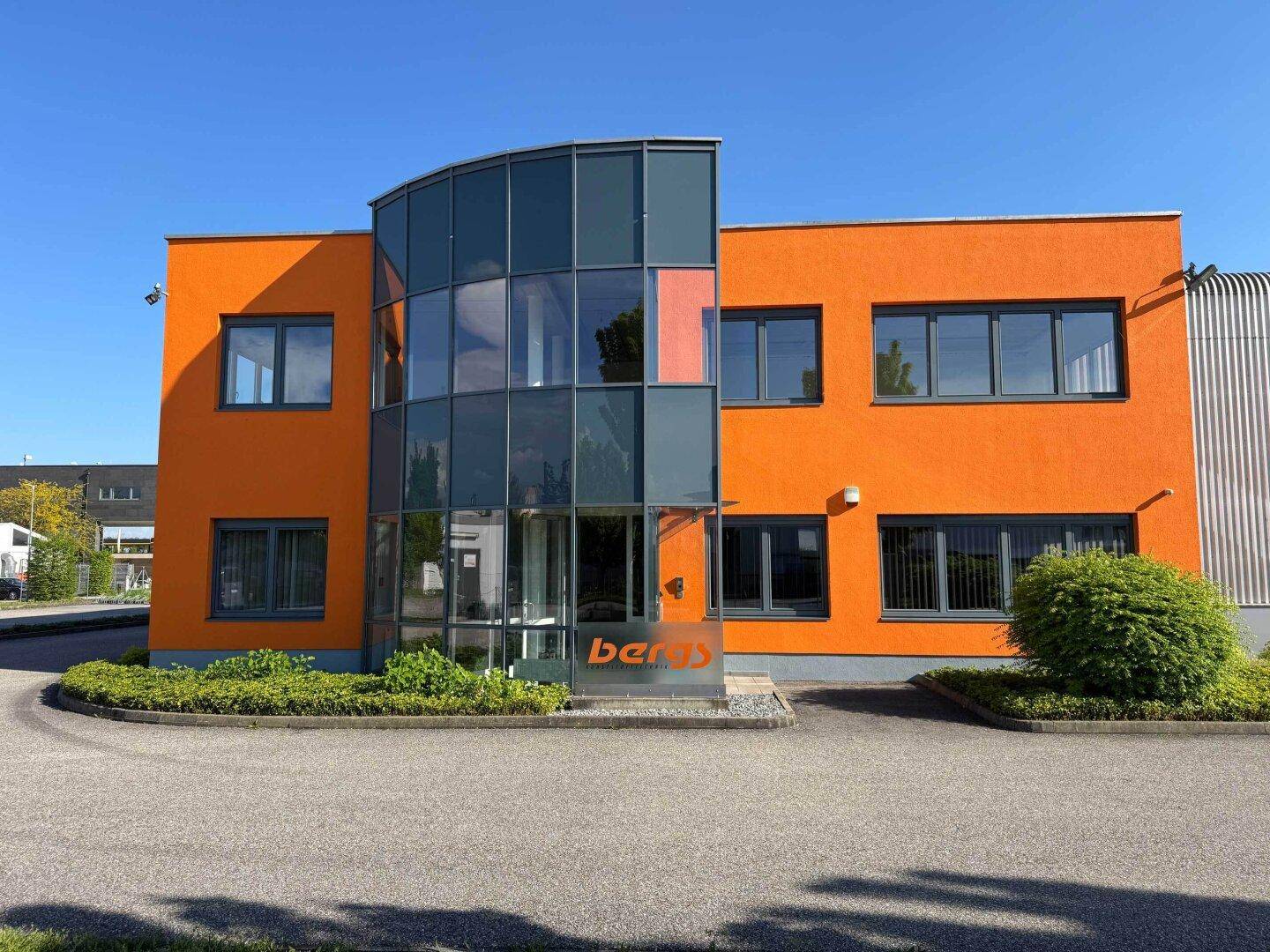 Frontansicht des orangefarbenen Bürotrakts mit moderner Glasfassade und Eingangsbereich.