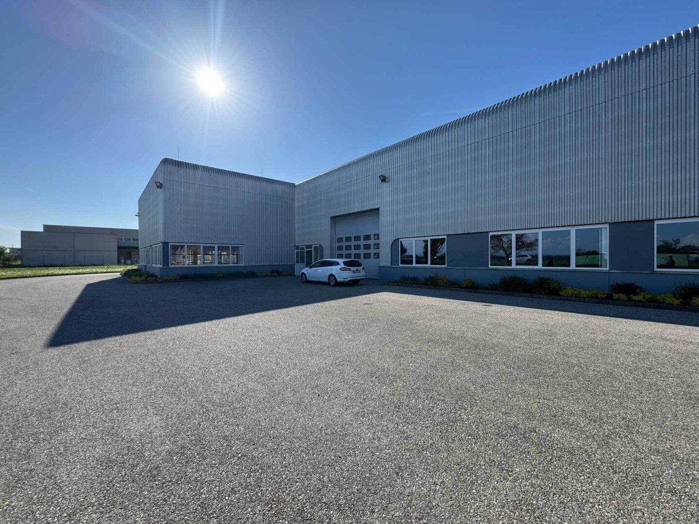 Seitenansicht des Industriegebäudes mit Laderampe und großem asphaltierten Parkplatz bei Sonnenschein.