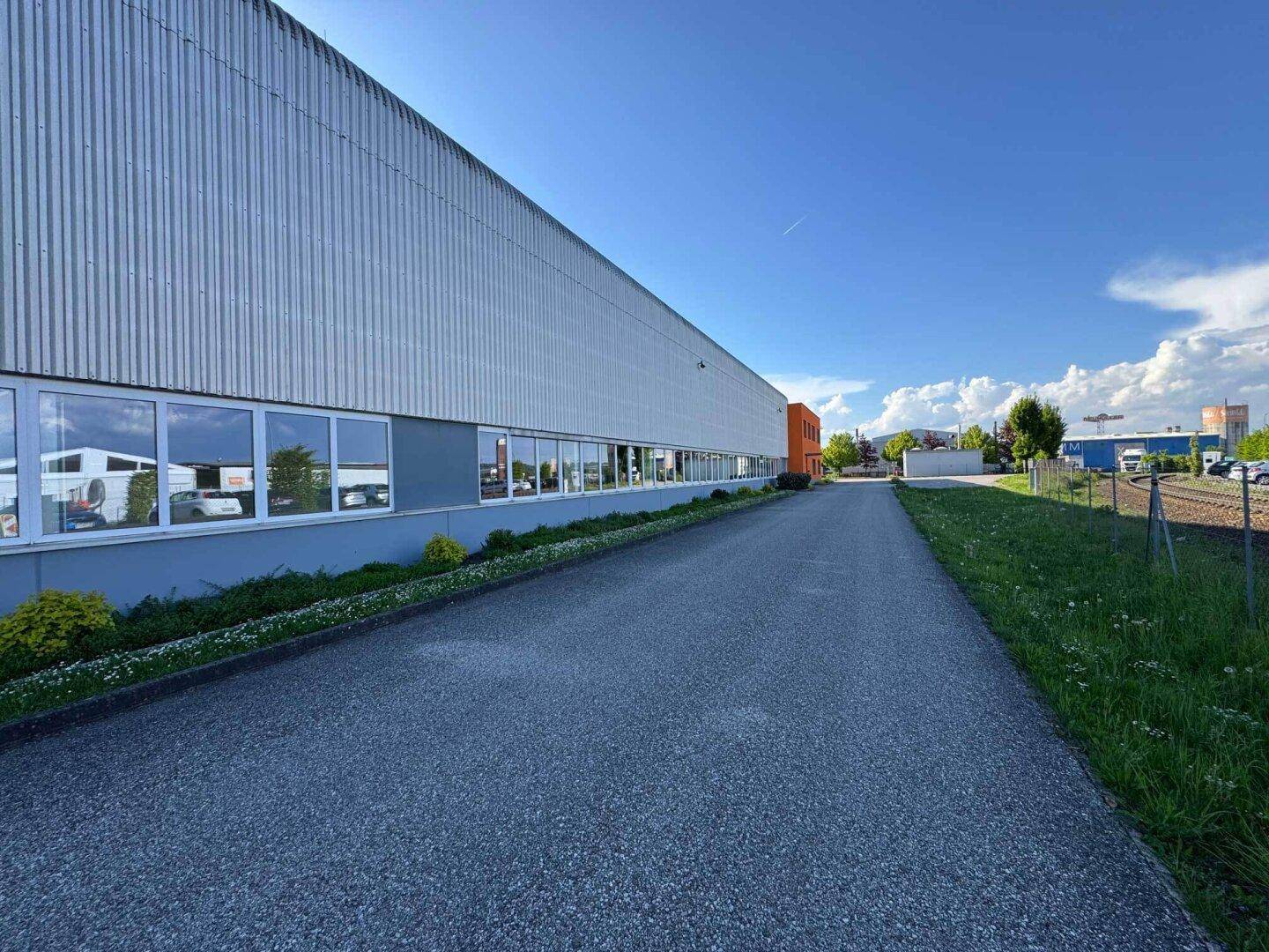 Lange Seitenansicht des Industriegebäudes mit Fensterreihen und Zufahrtsweg.