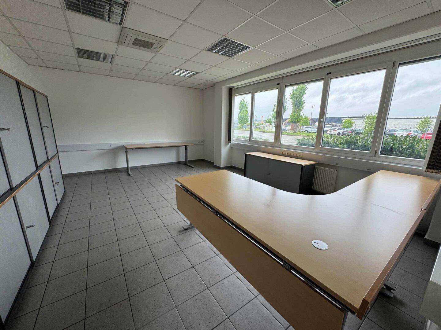 Geräumiges Büro mit großem Schreibtisch, Einbauschränken und weitem Ausblick durch die Fenster.