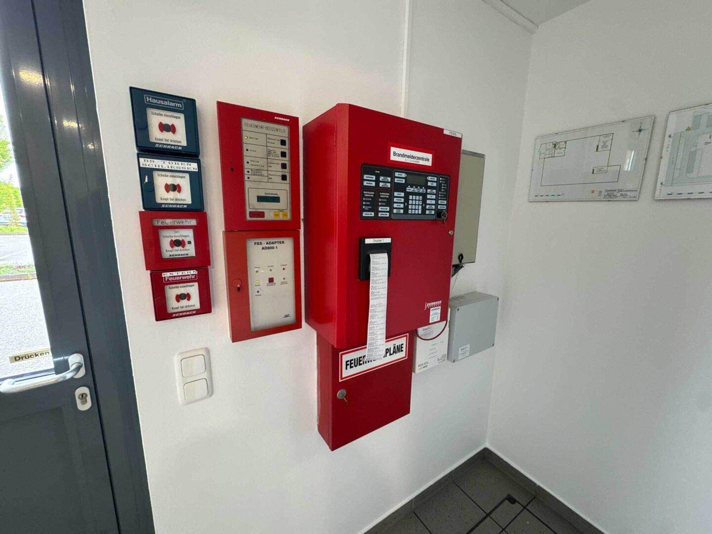 Wandmontierte Brandmeldezentrale und weitere Sicherheitssysteme in einem Flurbereich.