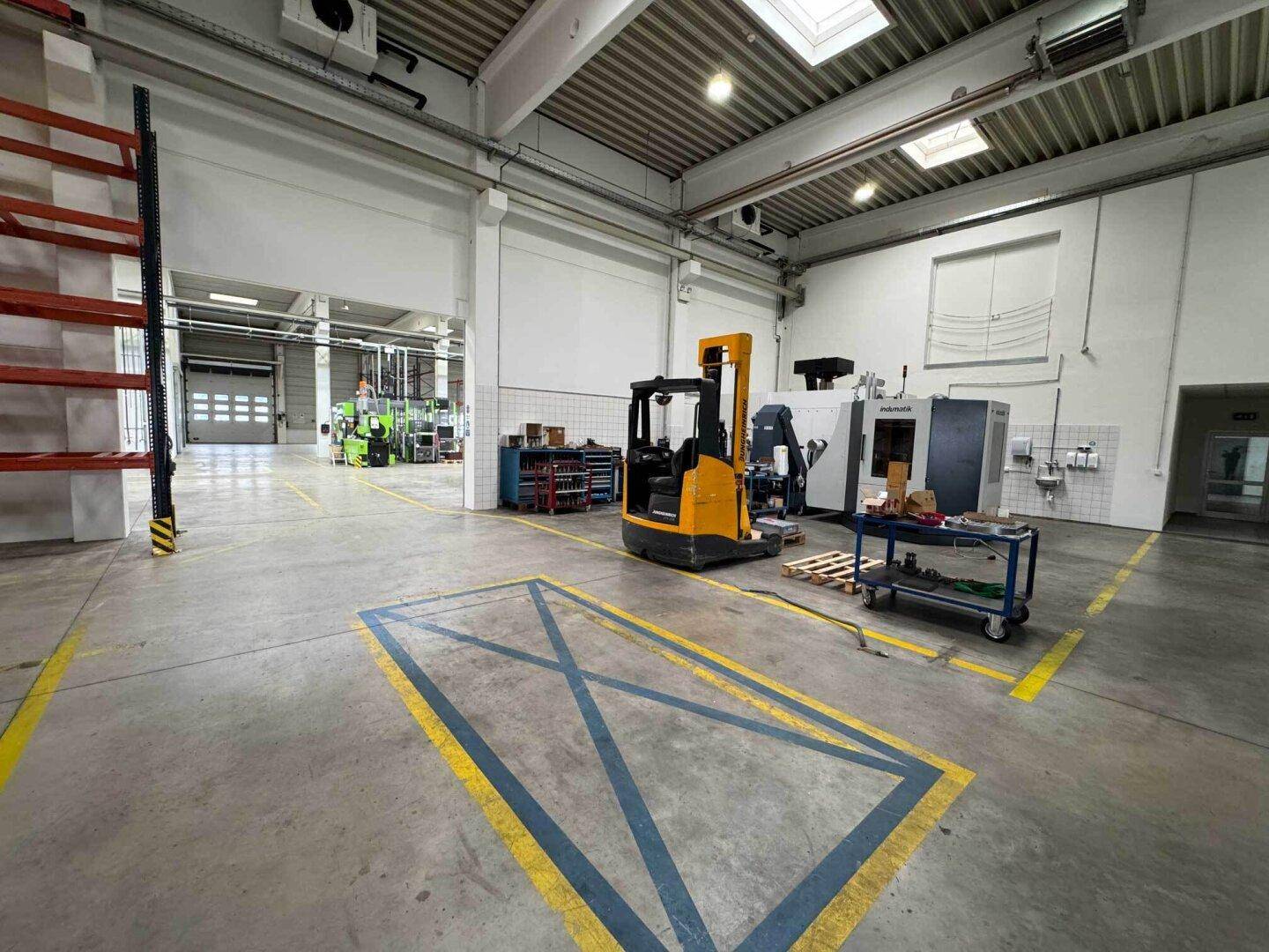 Geräumige Produktionshalle mit Gabelstapler, Maschinen und markierten Bodenbereichen.