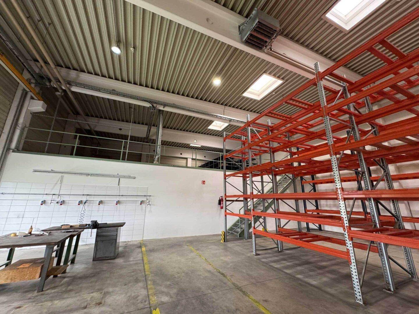 Geräumige Lagerhalle mit hohen Decken, Regalsystemen und einem Zwischengeschoss für zusätzliche Arbeitsflächen.