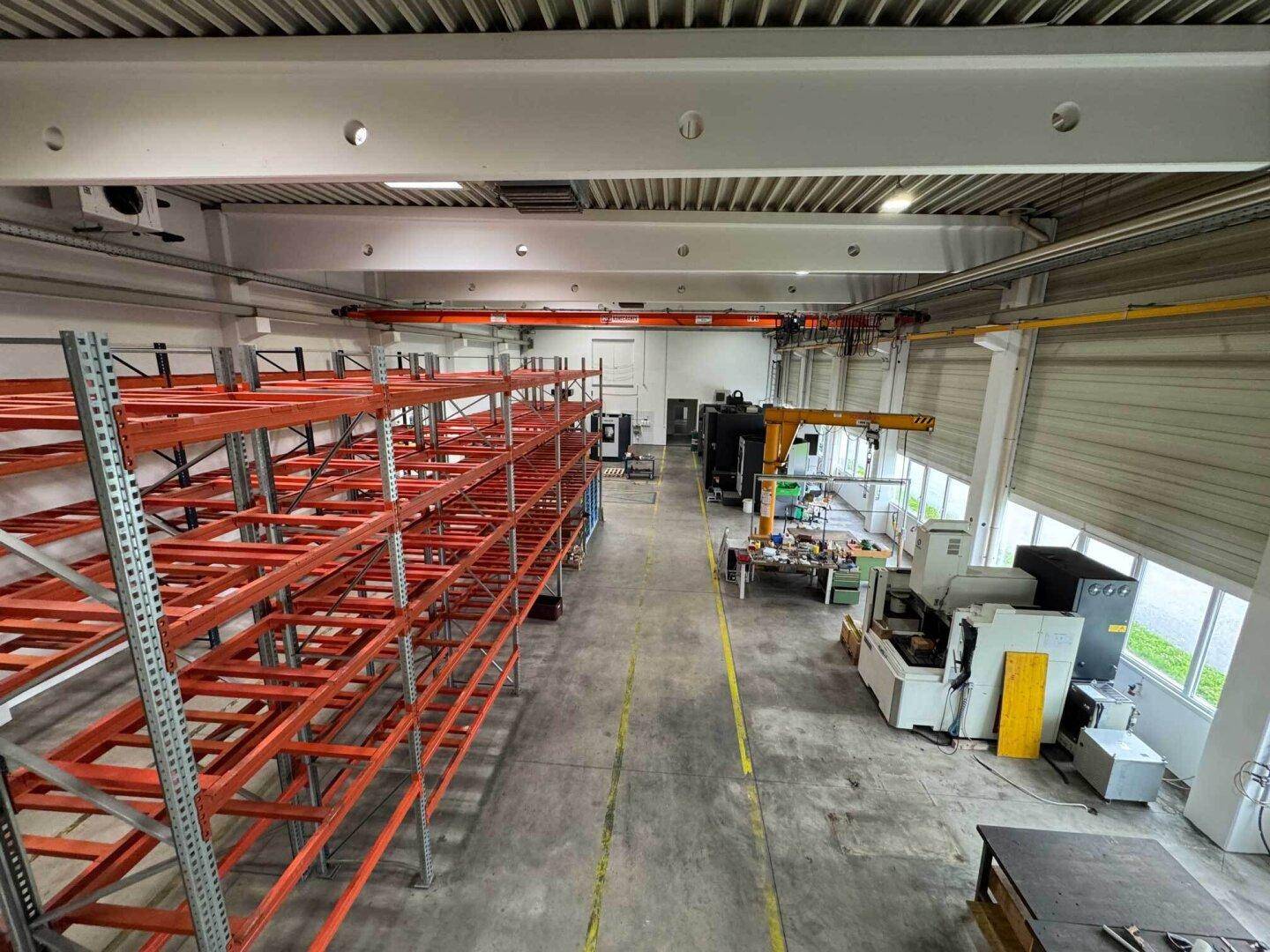Weitläufige Produktionshalle mit hohen Regalen, Maschinen und einem Kran unter der Decke.