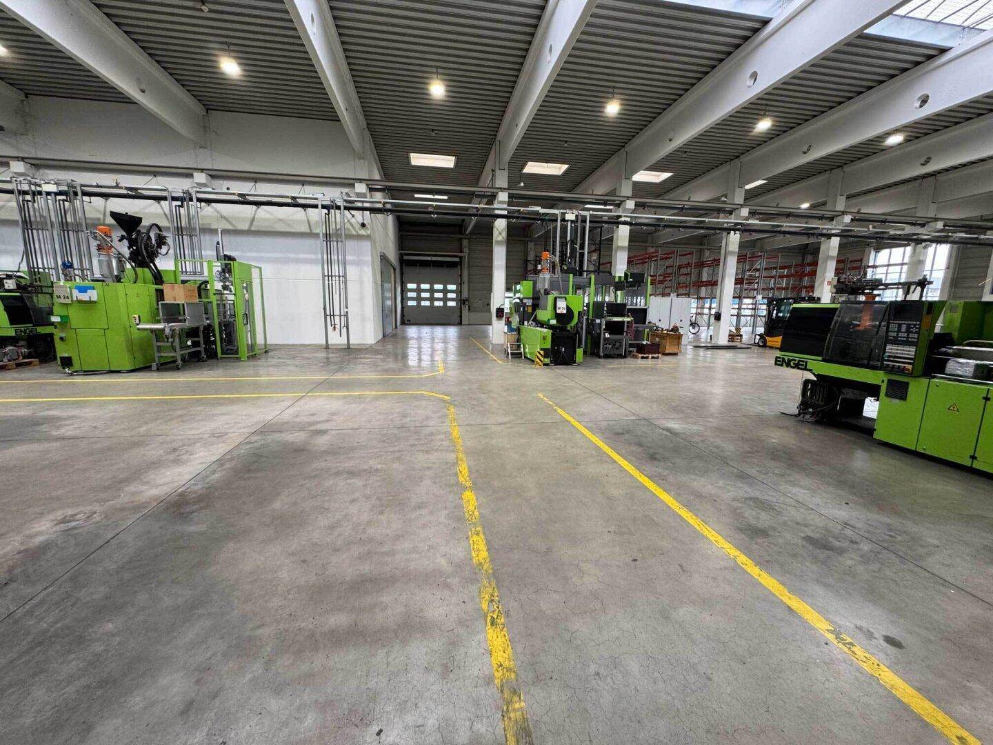 Weitläufige Produktionshalle mit mehreren Maschinen, gelben Bodenmarkierungen und einem großen Rolltor.