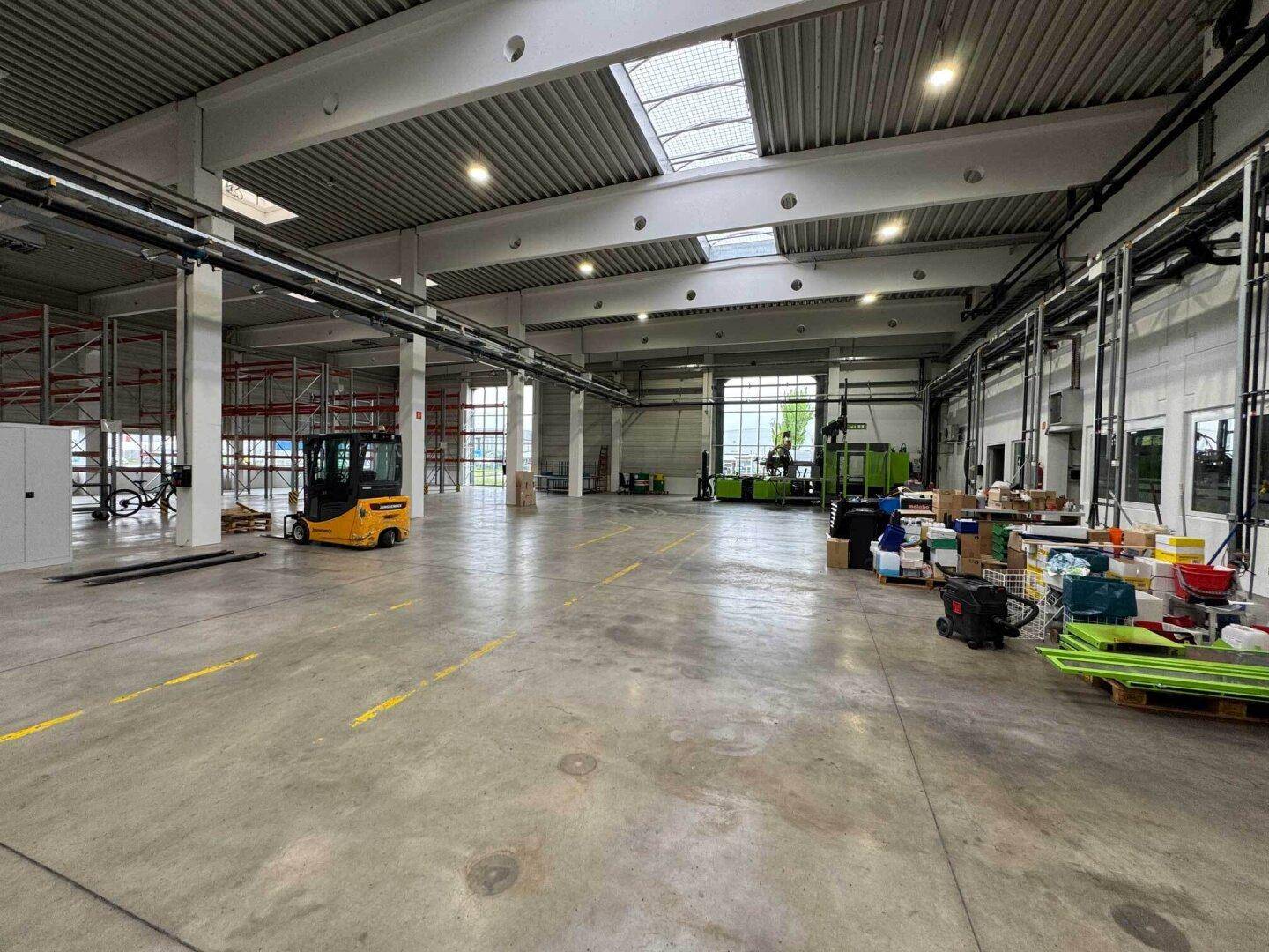 Große, helle Produktionshalle mit Maschinen, Gabelstapler und hohen Decken mit Oberlichtern.