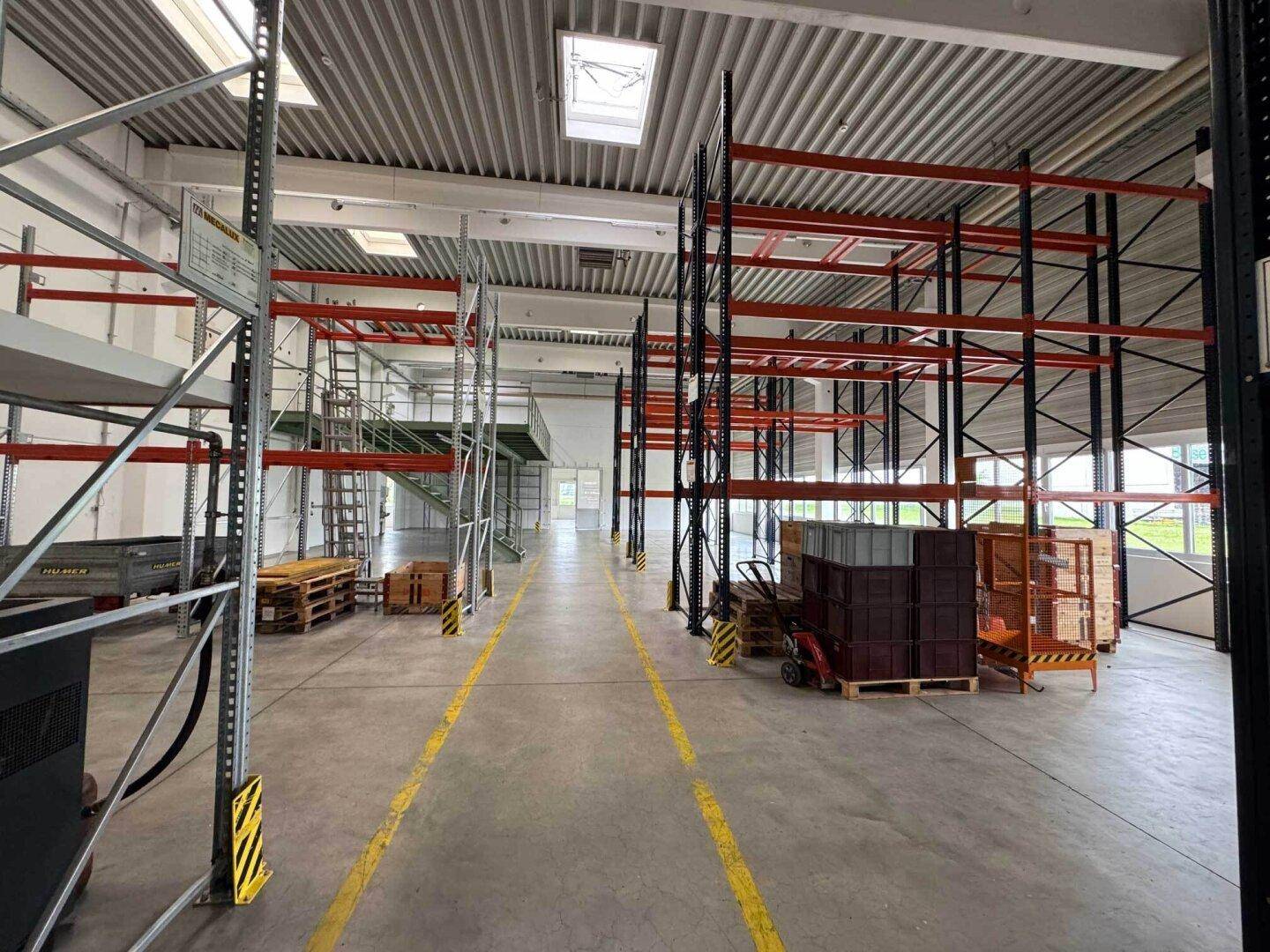Weitläufige Lagerhalle mit hohen Regalen, einer Zwischenebene und großzügigem Betonboden.
