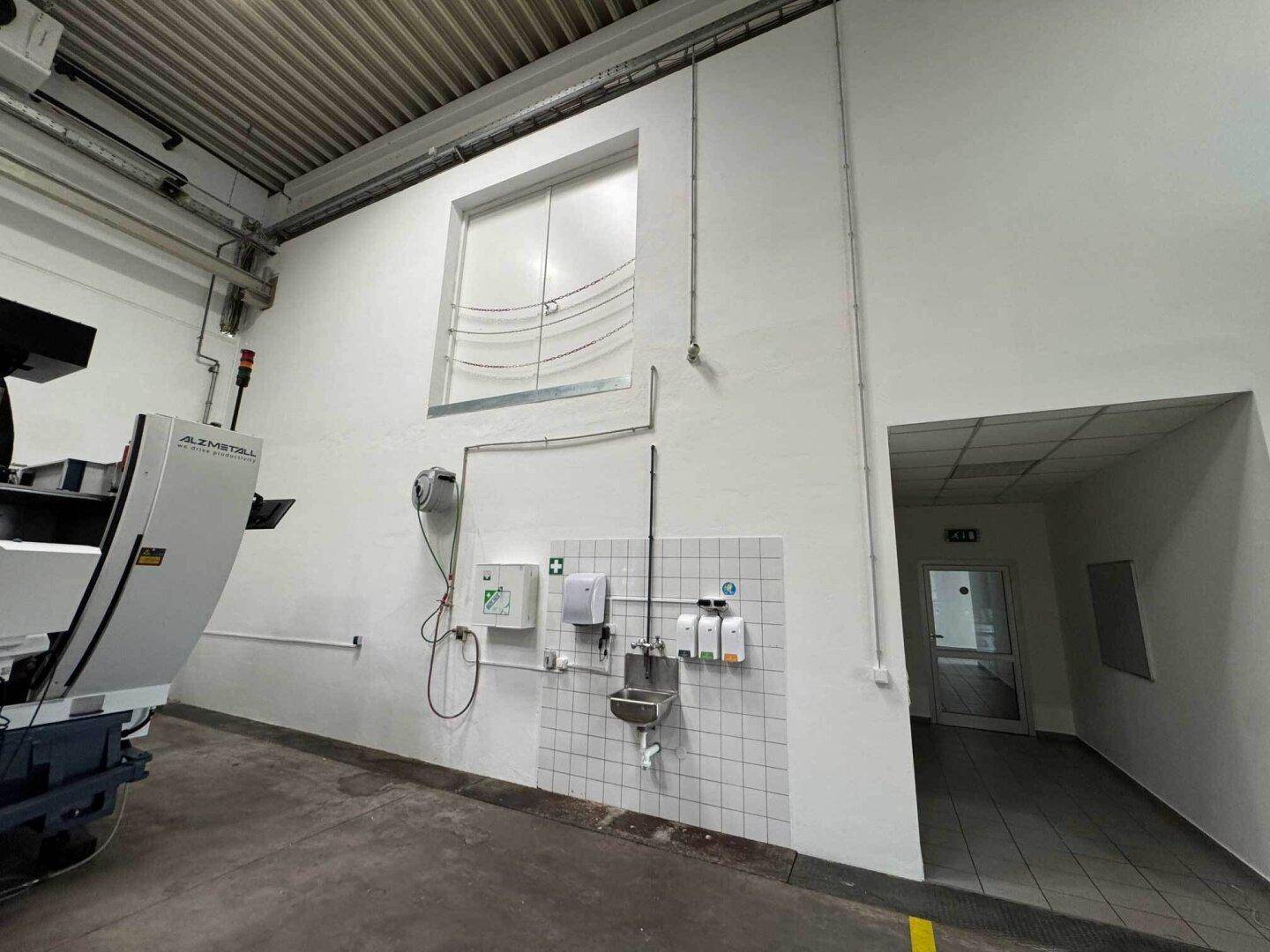 Bereich in der Lagerhalle mit Erste-Hilfe-Station, Waschbecken und Zugang zu weiteren Räumen.