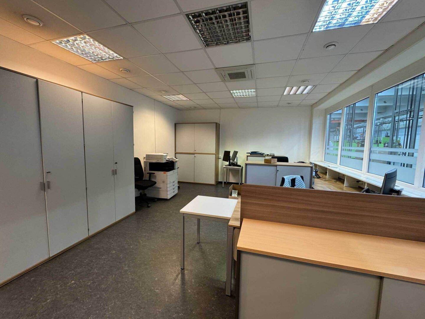 Modernes Büro mit Teppichboden, Einbauschränken und großen Fenstern, die viel Licht spenden.
