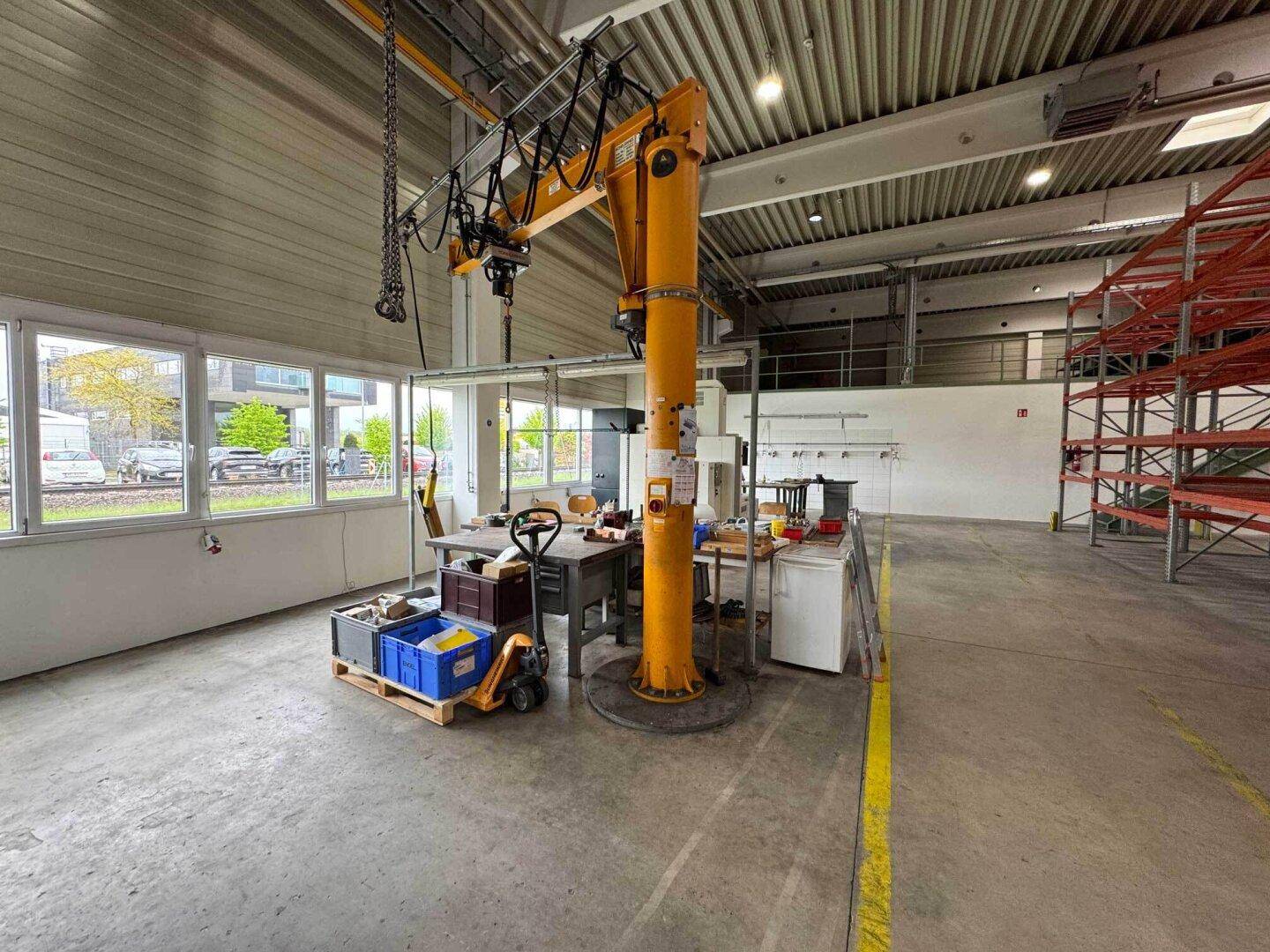 Arbeitsbereich in der Halle mit Werkbänken, einem Schwenkkran und großen Fenstern mit Blick nach draußen.