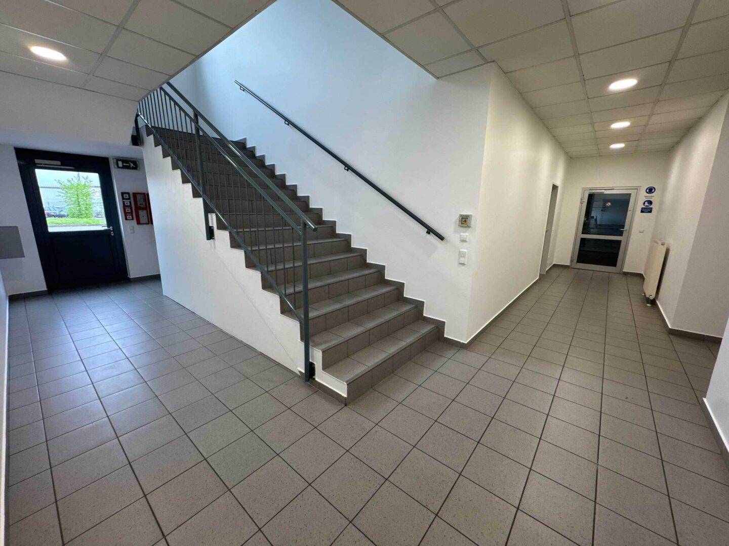 Geräumiger Flur mit Treppenaufgang, Fliesenboden und Zugang zu verschiedenen Bereichen.