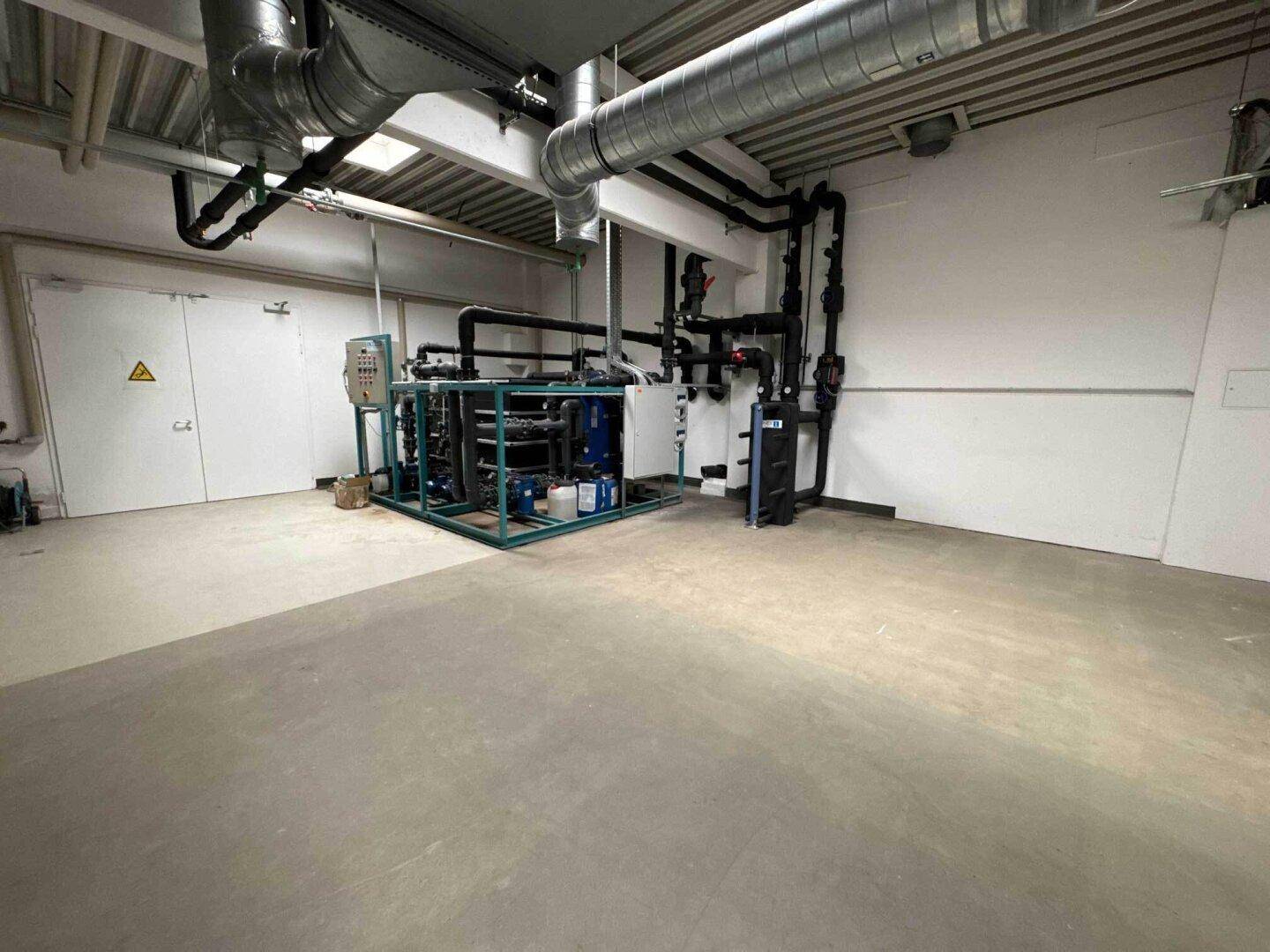 Technikraum mit großer Industrieanlage, Rohrleitungen und Betonboden für den Betrieb.