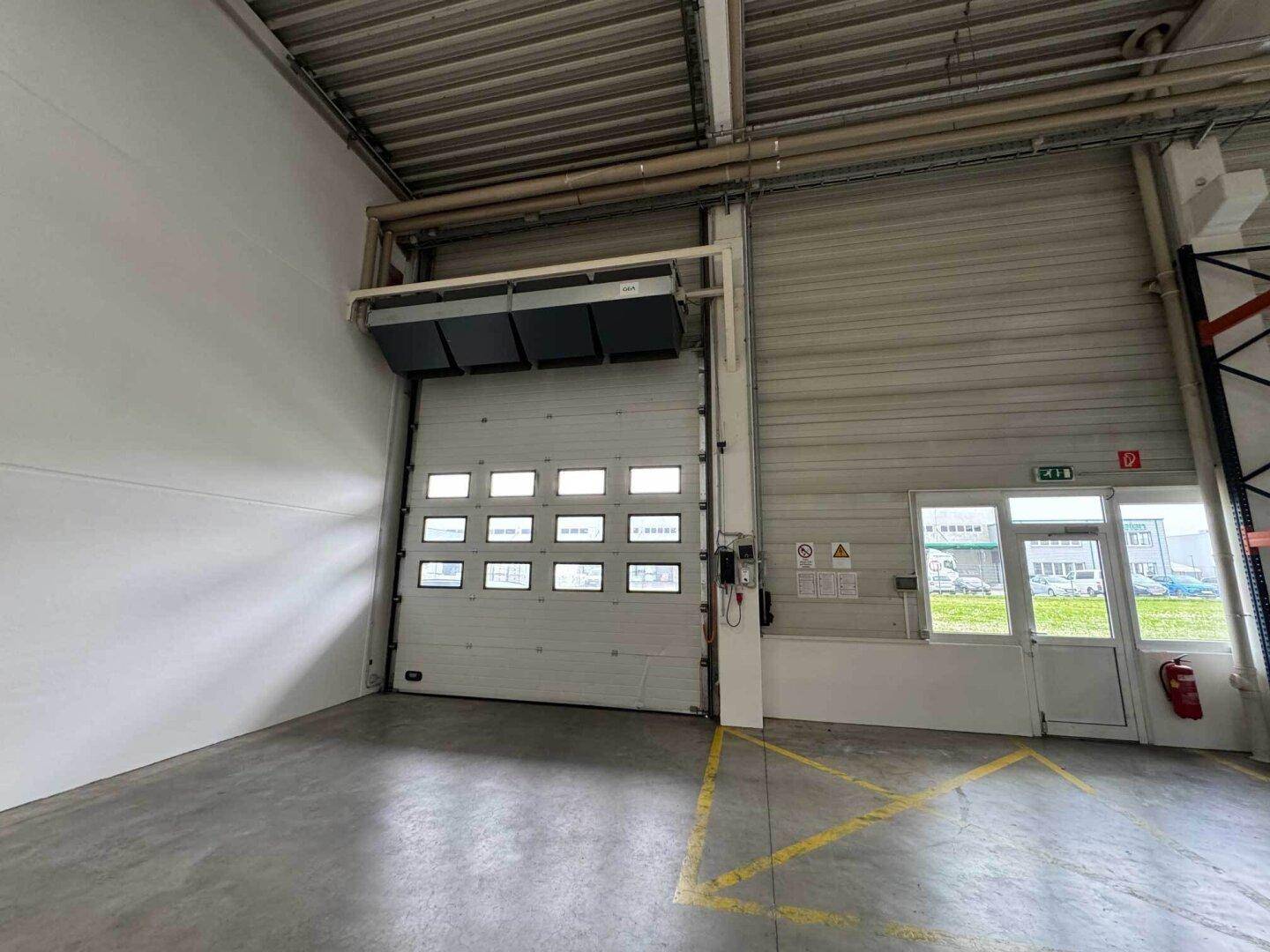 Sektionaltor mit integrierten Fenstern und einer darüberliegenden Heizung in einer hellen Industriehalle.
