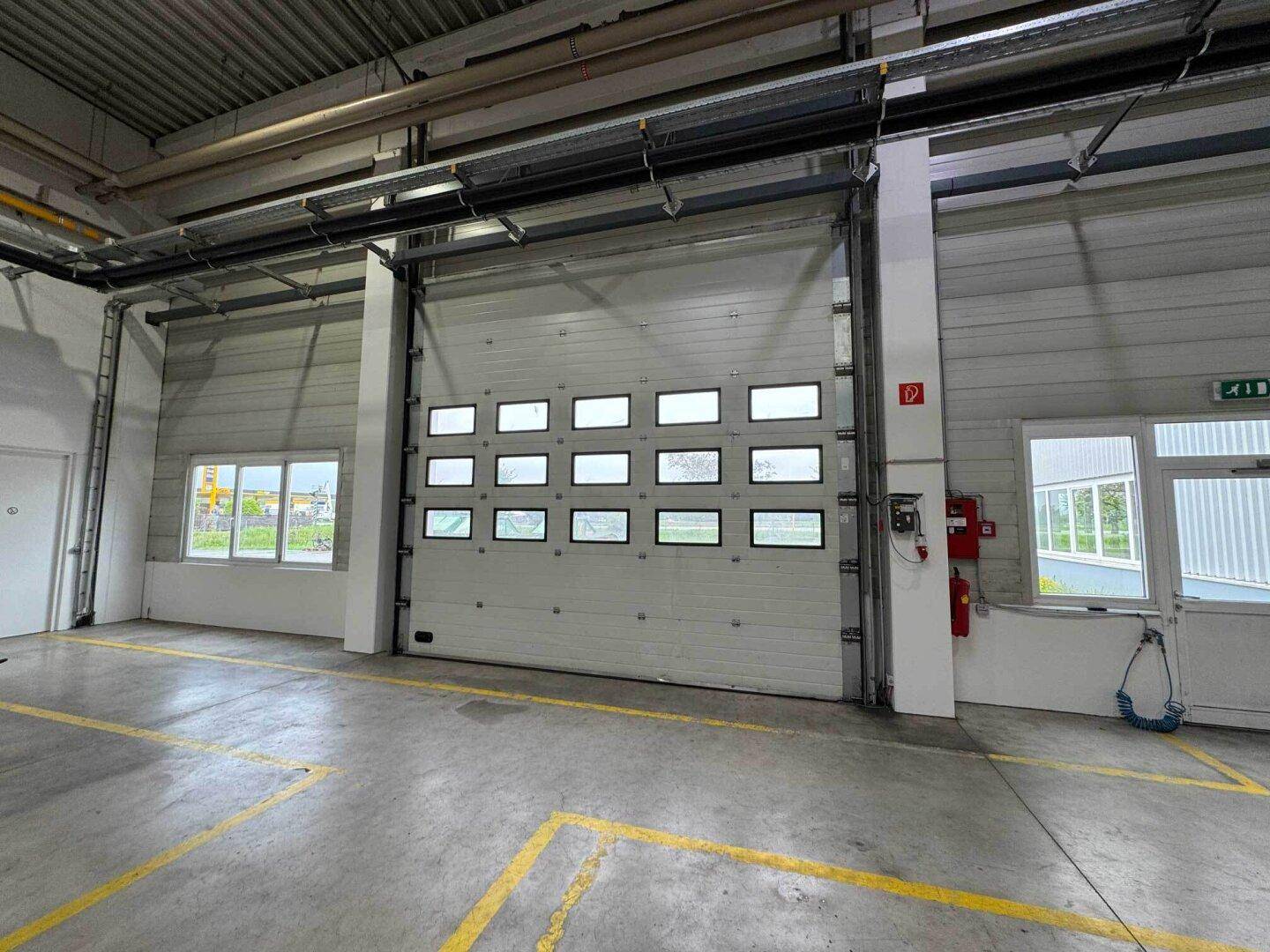Großes Sektionaltor mit Fenstern in einer Industriehalle, umgeben von weißen Wänden und kleineren Fenstern.