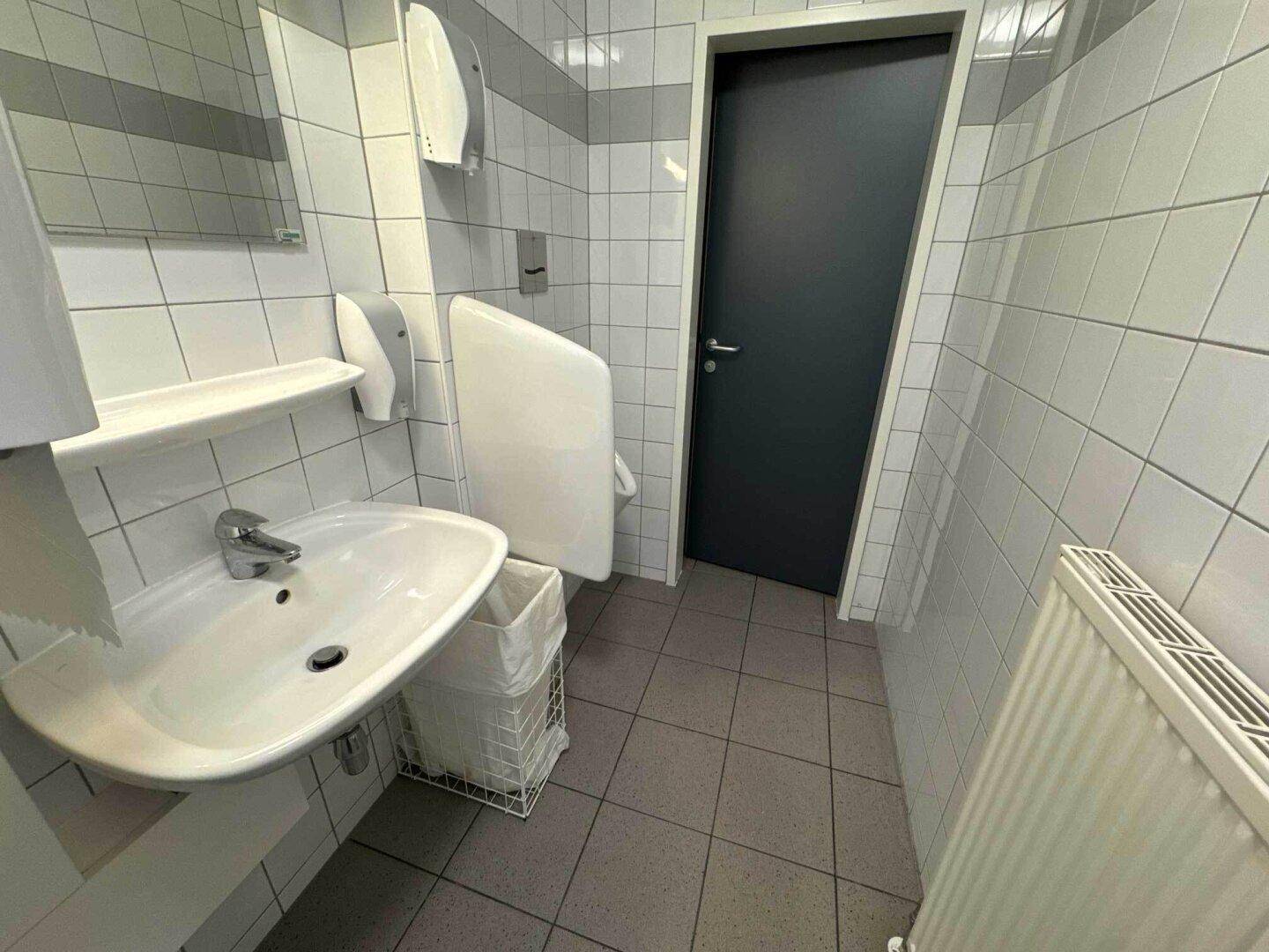 Toilettenraum mit Urinal, Waschbecken und gefliesten Wänden und Boden.