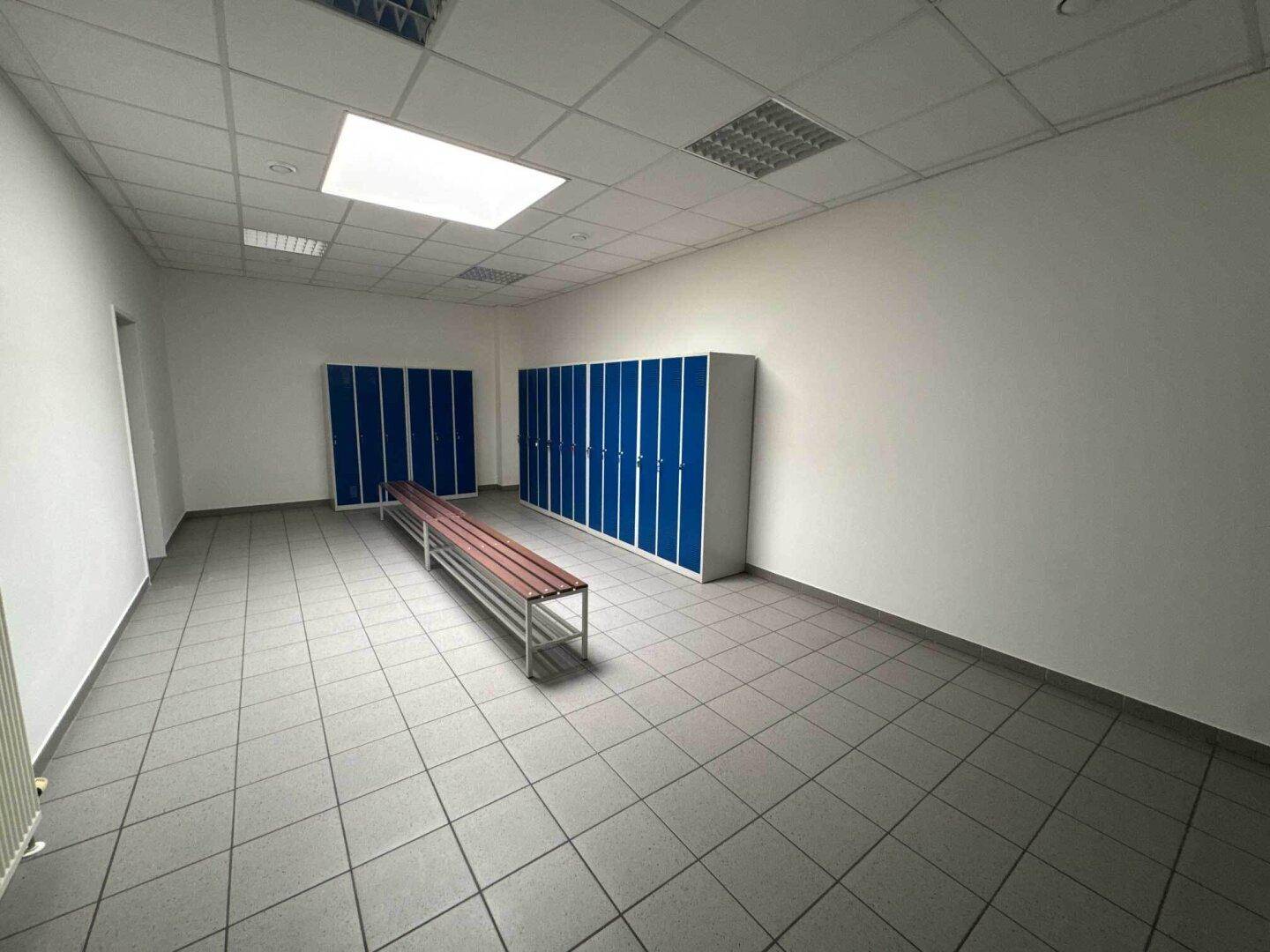 Umkleideraum mit blauen Spinden und einer Sitzbank, ideal für Mitarbeiter.