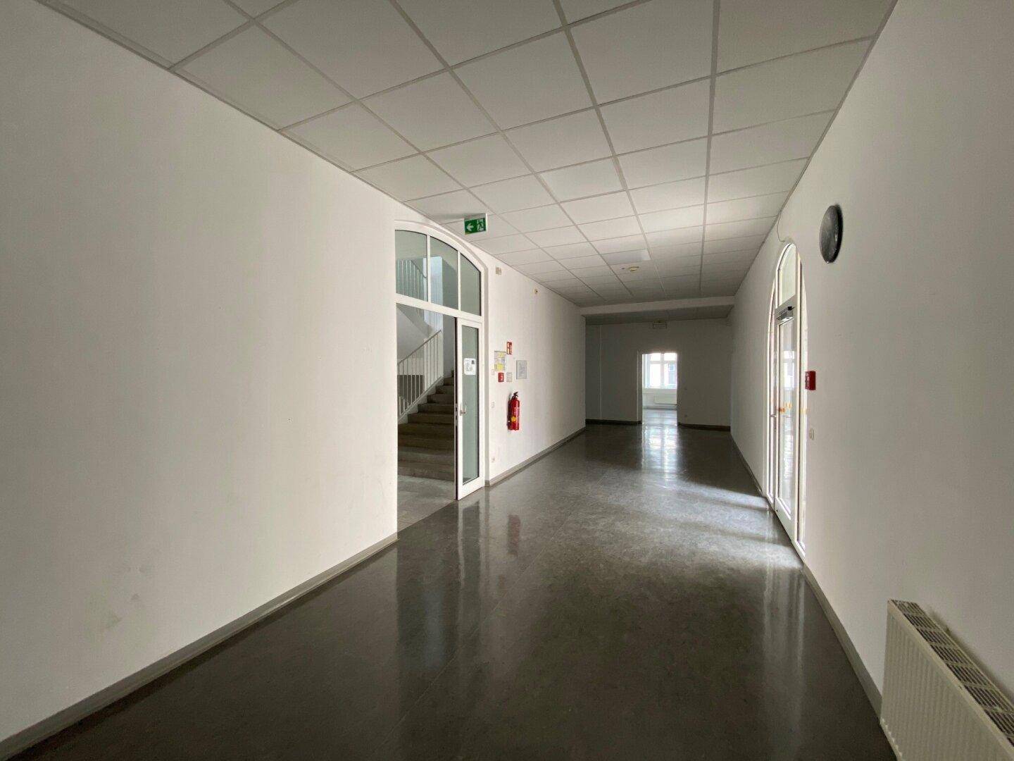 Langer, heller Flur mit glänzendem dunklem Boden, weißen Wänden und Türen, die zu weiteren Räumen führen.