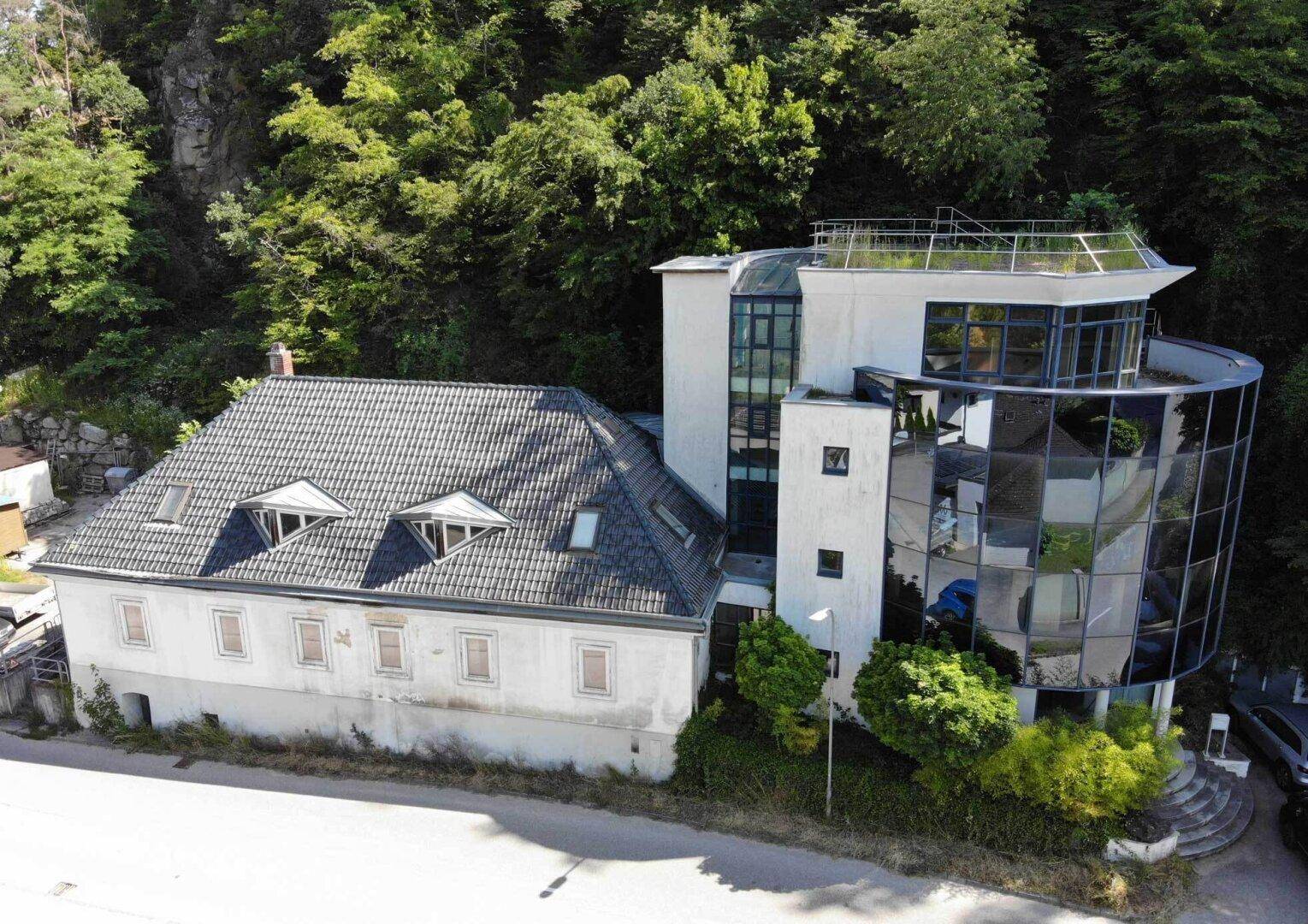 Architektonischer Kontrast zwischen einem modernen Gebäude mit Glasfassade und einem traditionellen Haus.