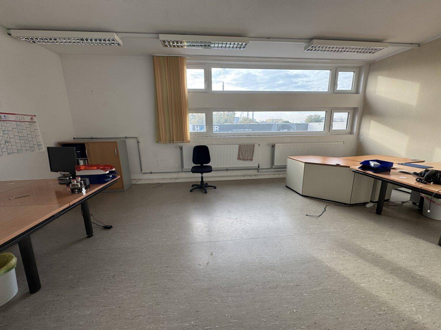 Geräumiges Büro mit großen Fenstern, mehreren Schreibtischen und Blick nach draußen.