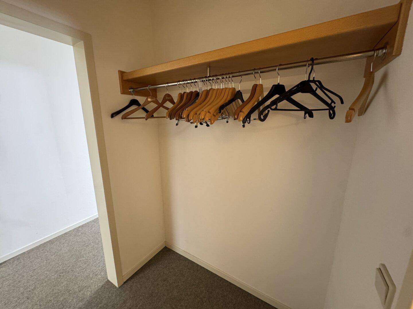 Kleiner begehbarer Kleiderschrank mit Kleiderstange und Teppichboden, ideal für Garderobe oder zusätzlichen Stauraum.