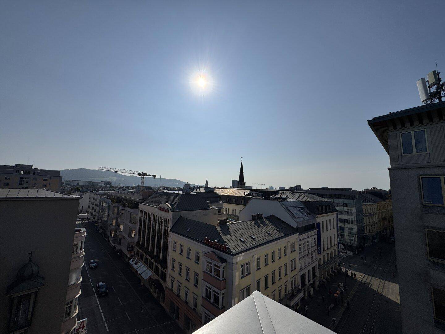 Weitblick über die Stadt mit historischen Dächern, belebten Straßen und sonnigem Himmel.