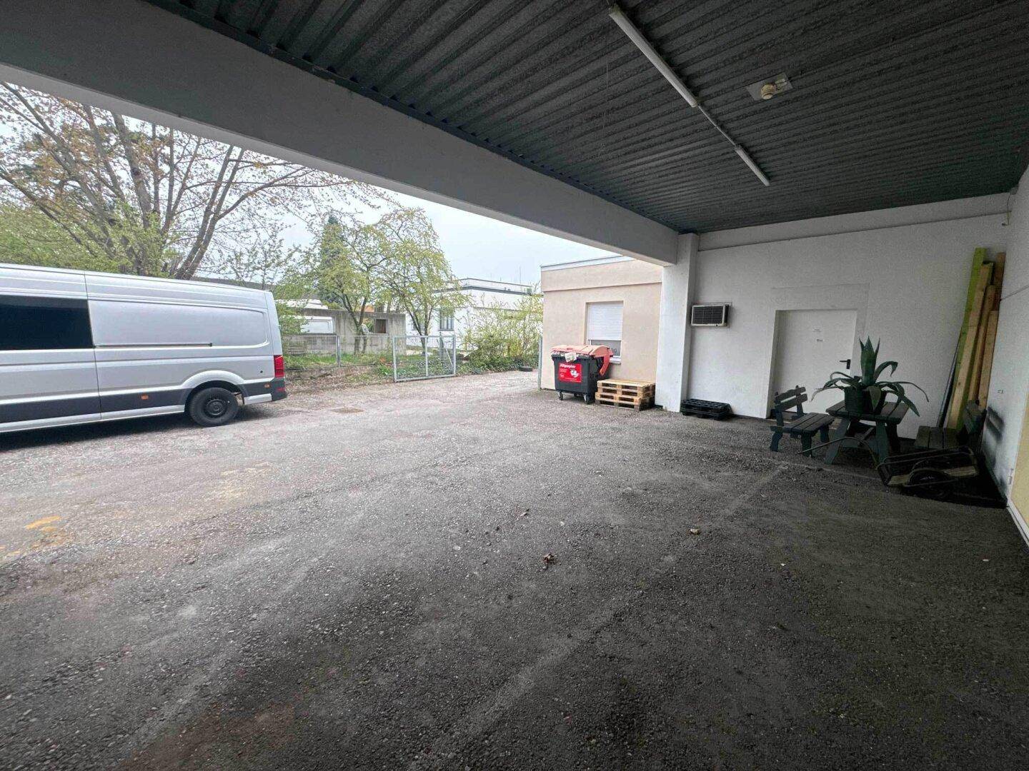 Überdachter Außenbereich mit Schotterboden, einem geparkten Lieferwagen und Blick auf das umliegende Gelände.