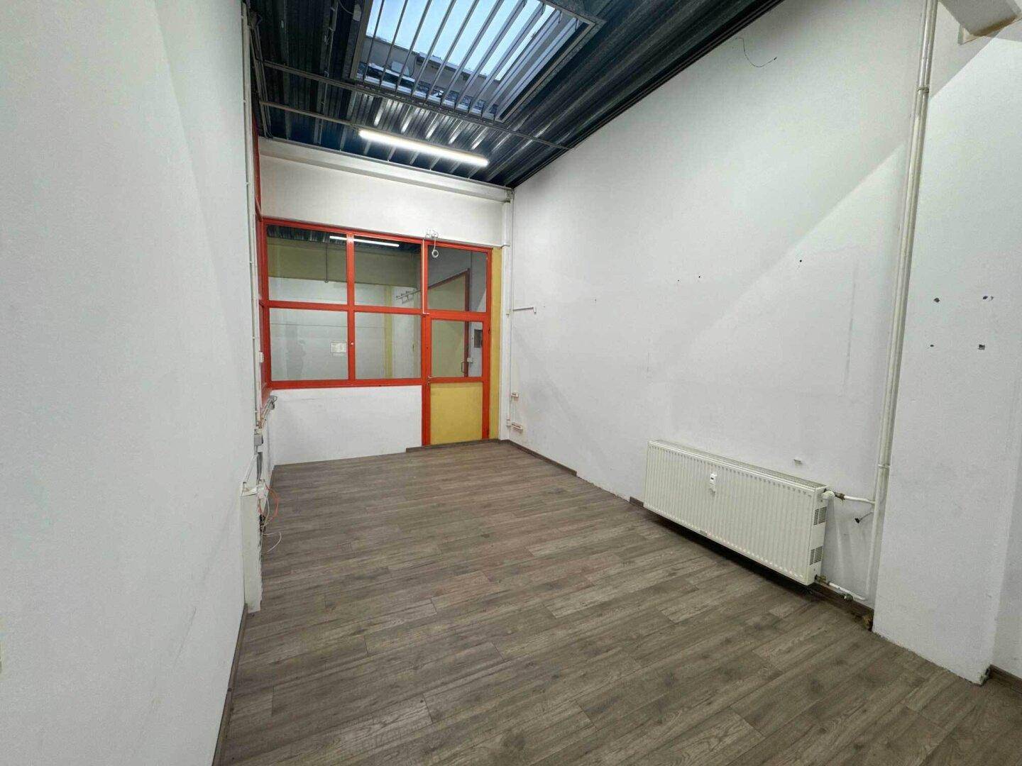 Heller Raum mit Laminatboden, Heizkörper und einem Fenster, das Tageslicht hereinlässt.