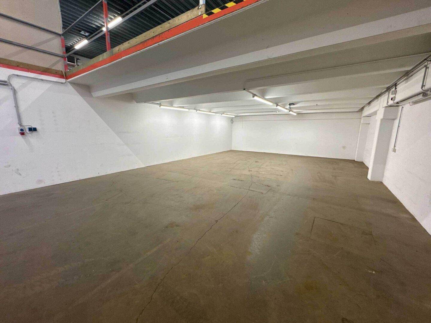 Großer, heller Lagerraum mit Betonboden, weißen Wänden und sichtbaren Deckenleuchten.