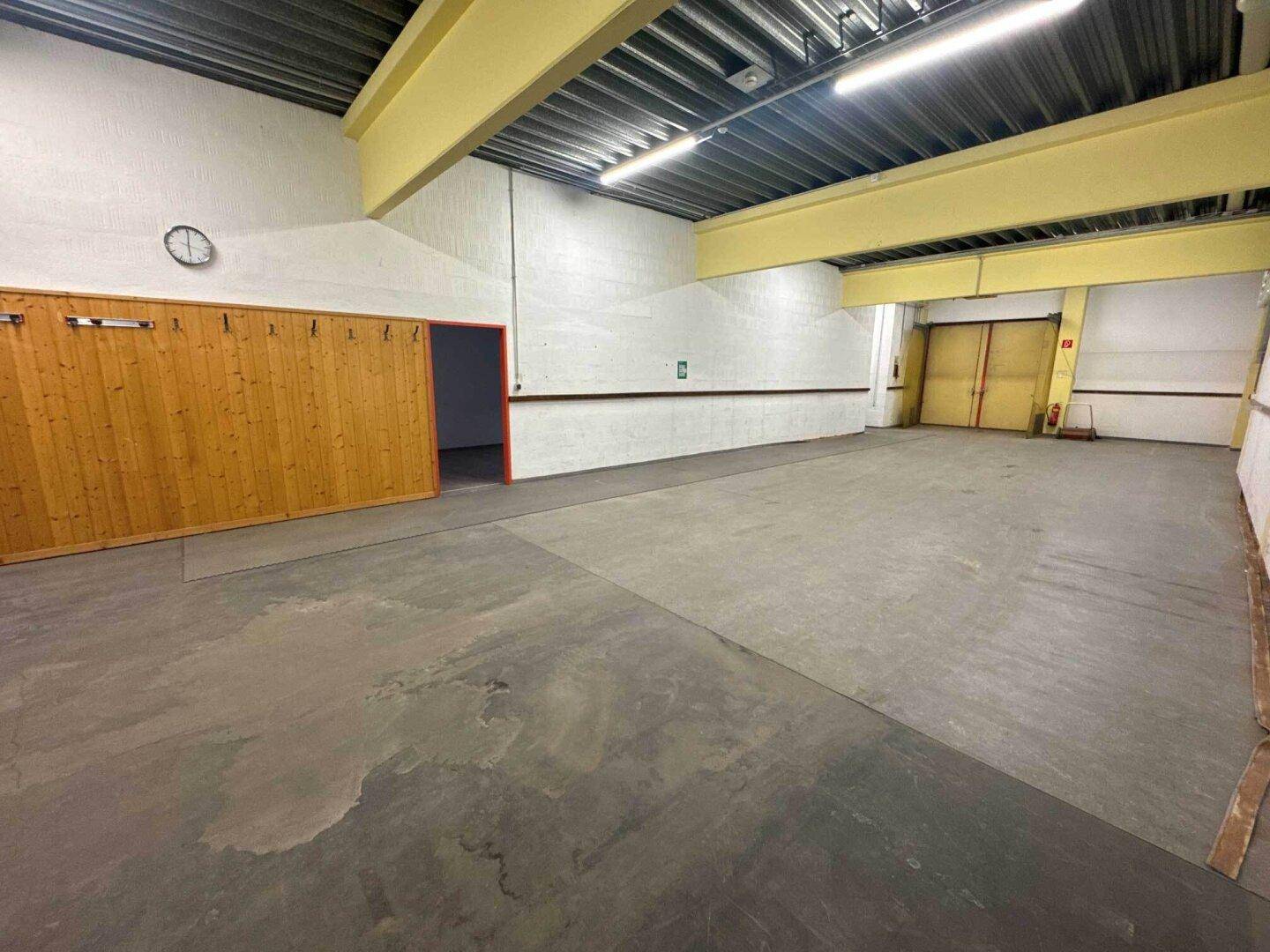 Weitläufige Lagerfläche mit Betonboden, hohen Decken und einer Holzwand im hinteren Bereich.