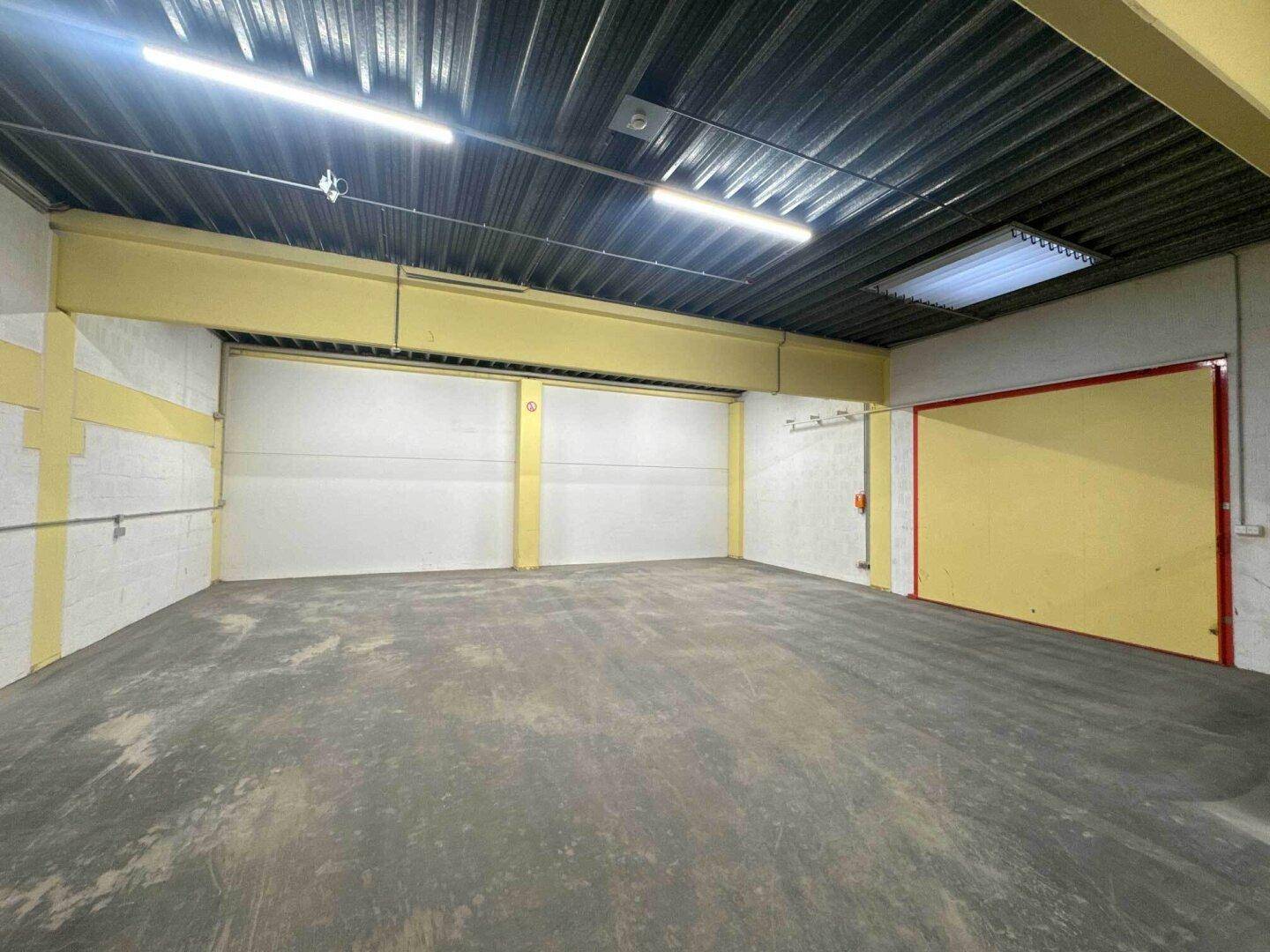 Geräumige Lagerhalle mit Betonboden, hohen Decken und mehreren großen Rolltoren für den Zugang.